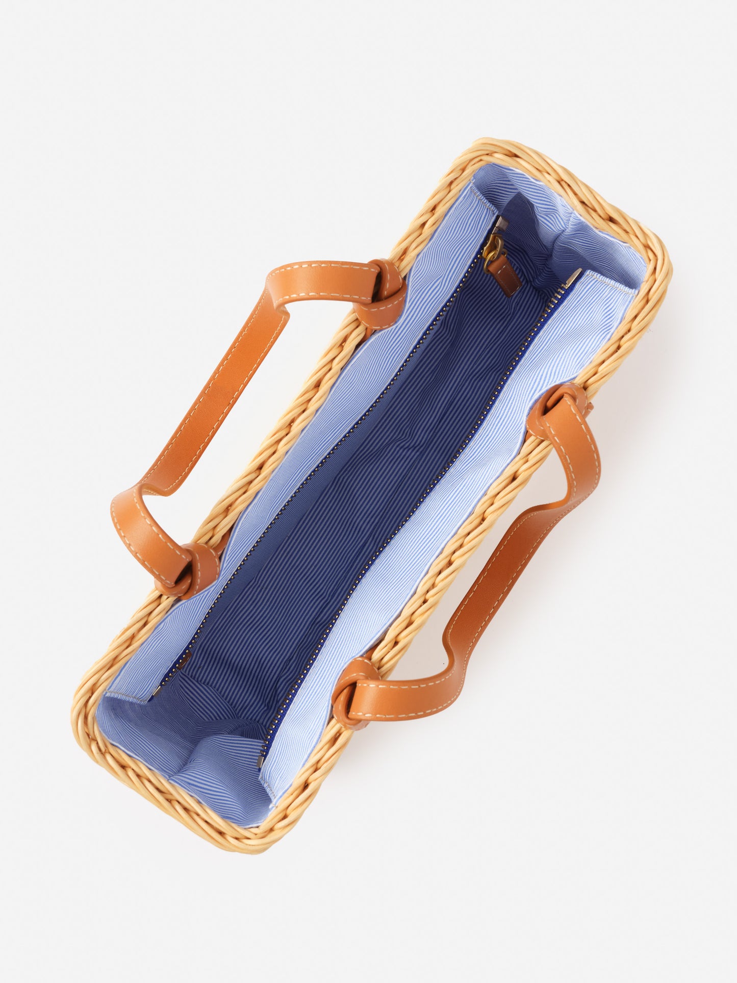Open top view of a Caroline Wicker Handbag by J.McLaughlin, featuring a woven wicker exterior, tan leather handles, and a blue striped fabric interior, combining effortlessly stylish design with enduring craftsmanship.