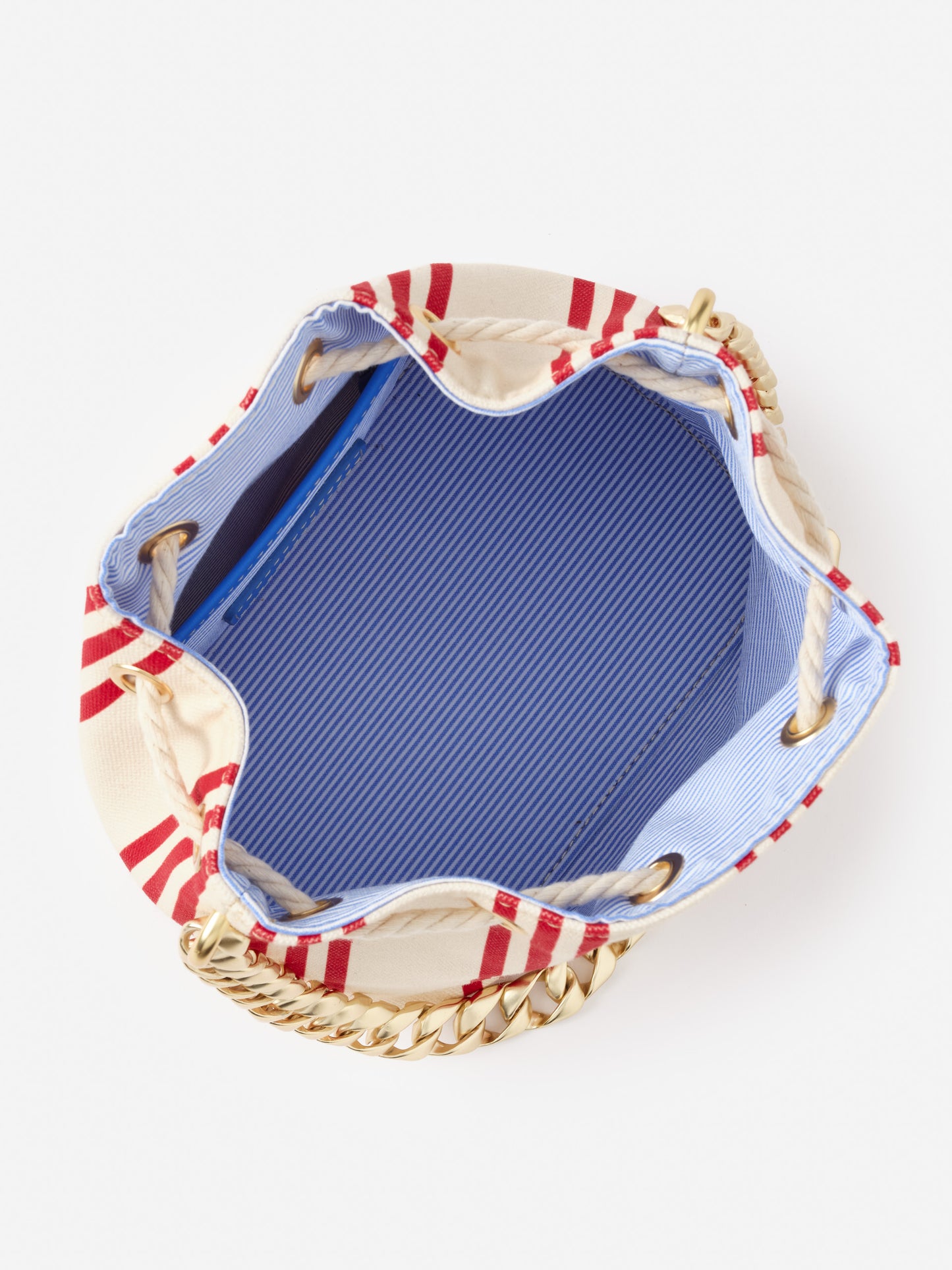 Open view of Daisy Canvas Bucket Bag in Stripe by J.McLaughlin showing blue striped interior lining, cream canvas exterior with red stripes, rope drawstring closure, and gold chain handle, embodying effortlessly stylish, enduring designs with a legacy of timeless fashion.