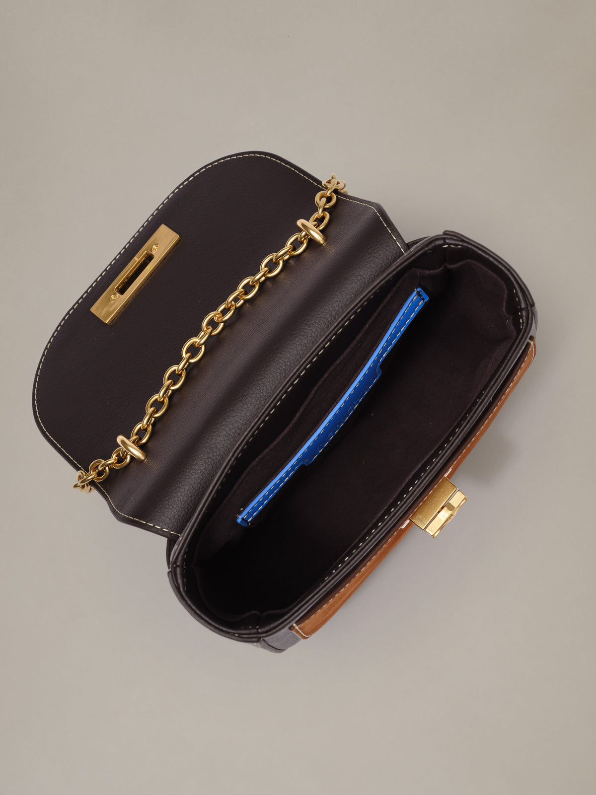 The Waverly Leather Handbag by J.McLaughlin shown open with a gold chain strap and spacious dark interior holding a blue item