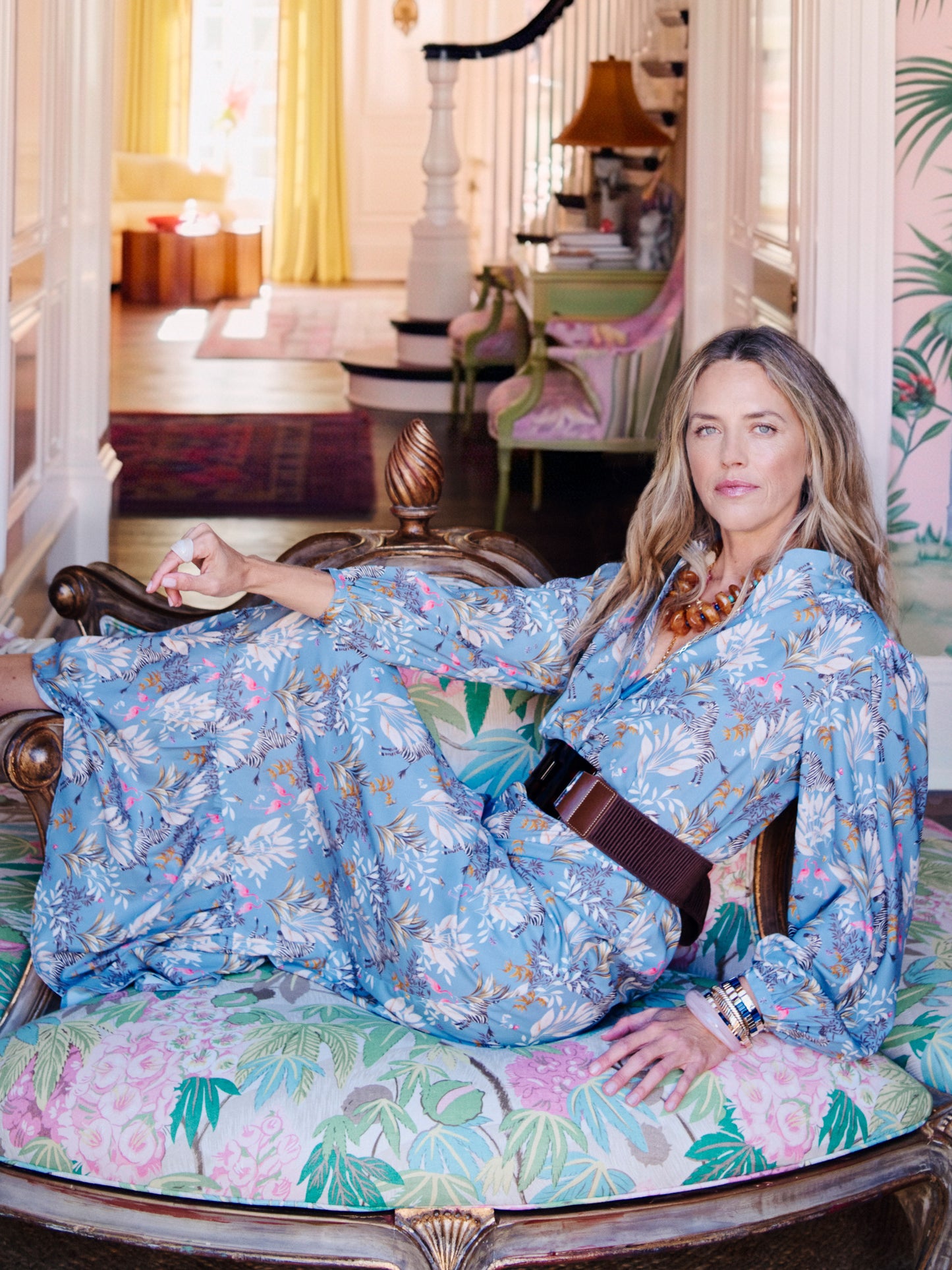 Woman lounging on a floral upholstered chair wearing a flowing blue patterned dress cinched at the waist with an Orsay Tortoise Belt by J.McLaughlin, showcasing effortlessly stylish, enduring designs and a legacy of timeless fashion at a destination for defining style, Life, Well-Lived.