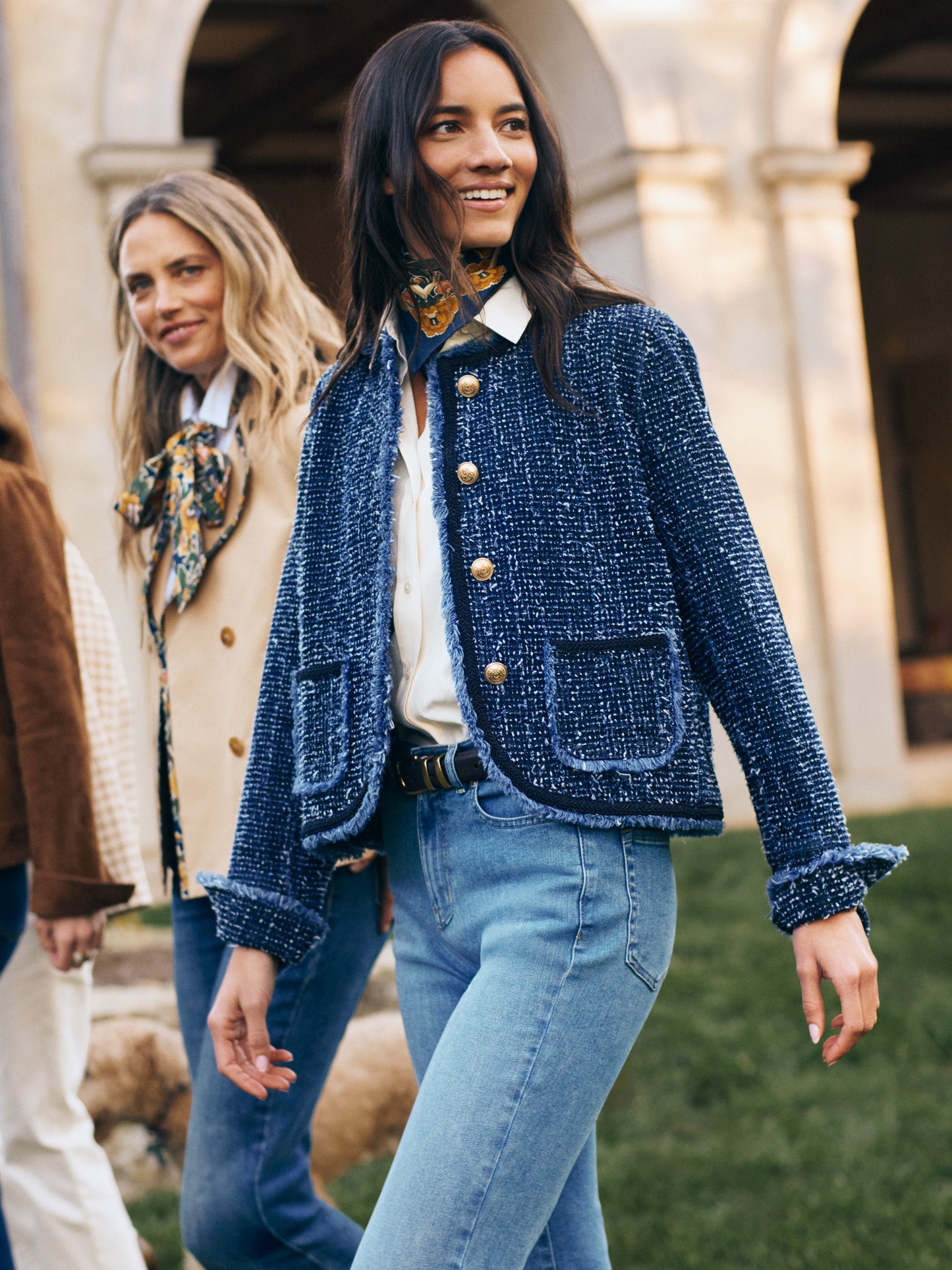 Woman wearing J.McLaughlin blue textured jacket, white blouse, jeans, and Nikka Silk Scarf in Bucolic Blooms Kerchief tied around her neck, embodying effortlessly stylish, enduring designs and a legacy of timeless fashion at a destination for defining style. Life, Well-Lived.