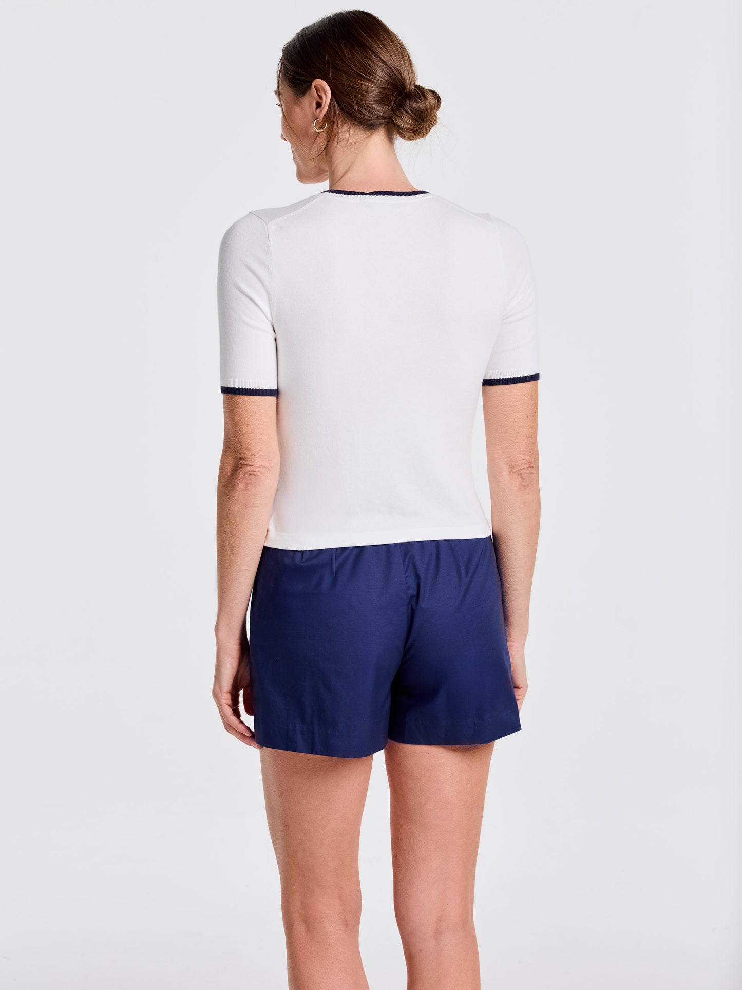 Woman seen from behind wearing a white Alyson Sweater Tee with navy trim and navy shorts, showcasing J.McLaughlin’s effortlessly stylish, enduring designs and innovative fabrics.