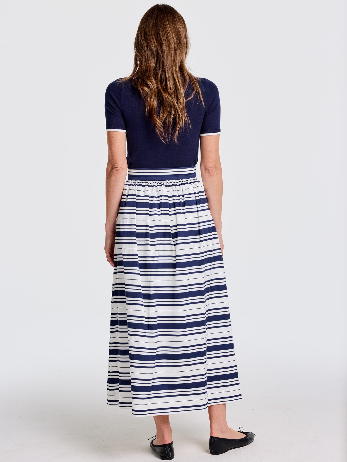 Woman wearing a Susie Skirt in Mariner Stripe by J.McLaughlin featuring bold navy and white stripes, paired with a navy short-sleeve top, showcasing effortlessly stylish, enduring designs in timeless fashion.