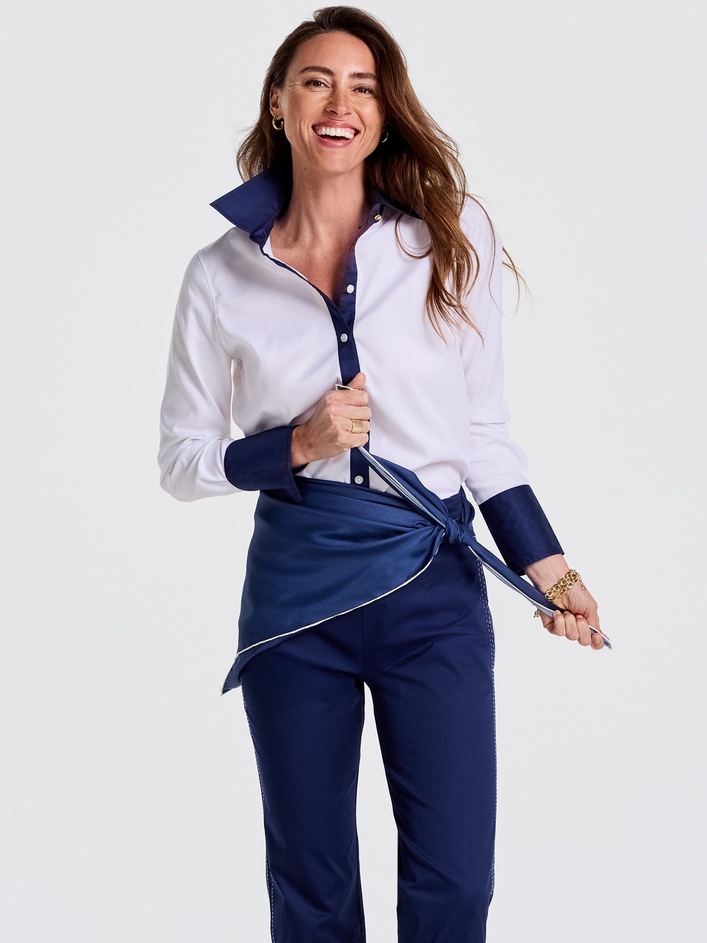 Woman wearing a crisp white and navy blouse with navy pants, tying a deep blue Kyleigh Silk Scarf from J.McLaughlin around her waist, showcasing effortlessly stylish, enduring designs in innovative fabrics, a legacy of timeless fashion. A destination for defining style. Life, Well-Lived.