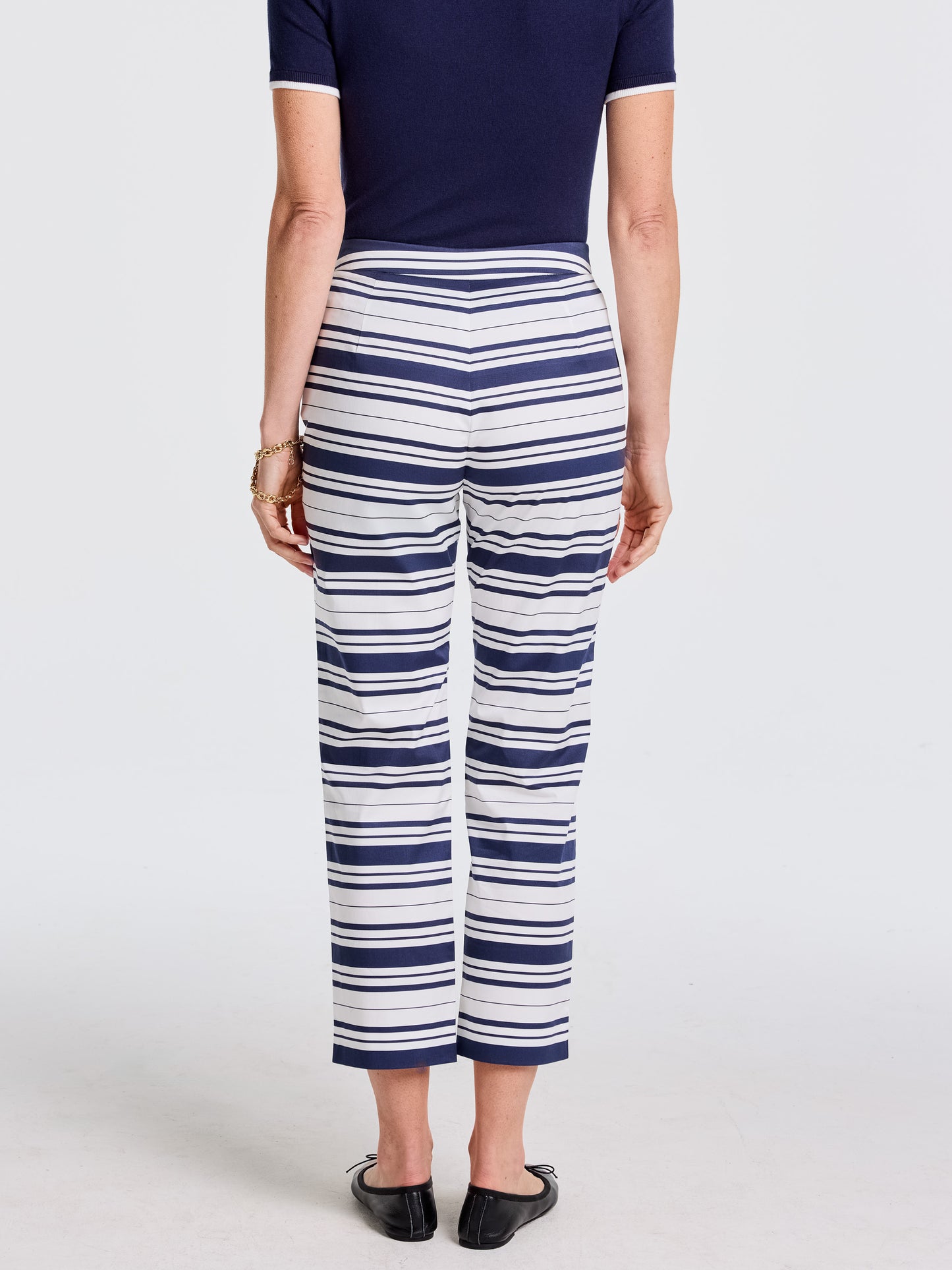 Woman wearing Betina Pants in Mariner Stripe by J.McLaughlin, featuring alternating navy and white stripes, paired with a navy top and black flats, showcasing effortlessly stylish, enduring designs, innovative fabrics, legacy of timeless fashion. A destination for defining style. Life, Well-Lived.