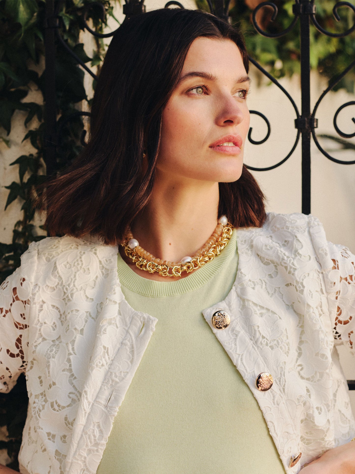 Woman wearing a white lace jacket and light green top showcasing the Intertwined Link Chain Necklace by J.McLaughlin, reflecting effortlessly stylish, enduring designs and a legacy of timeless fashion.