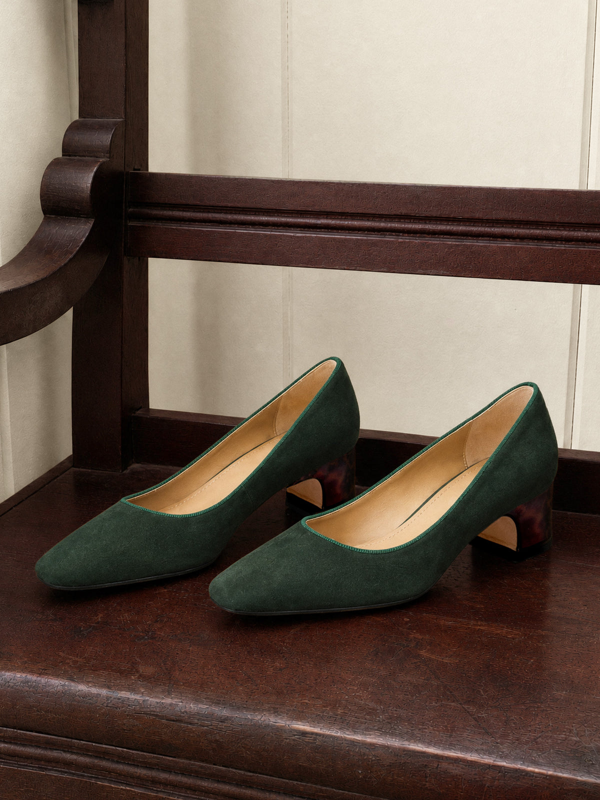 Josie Suede Pumps by J.McLaughlin in deep green suede with low tortoise pattern heels displayed on a classic wood bench