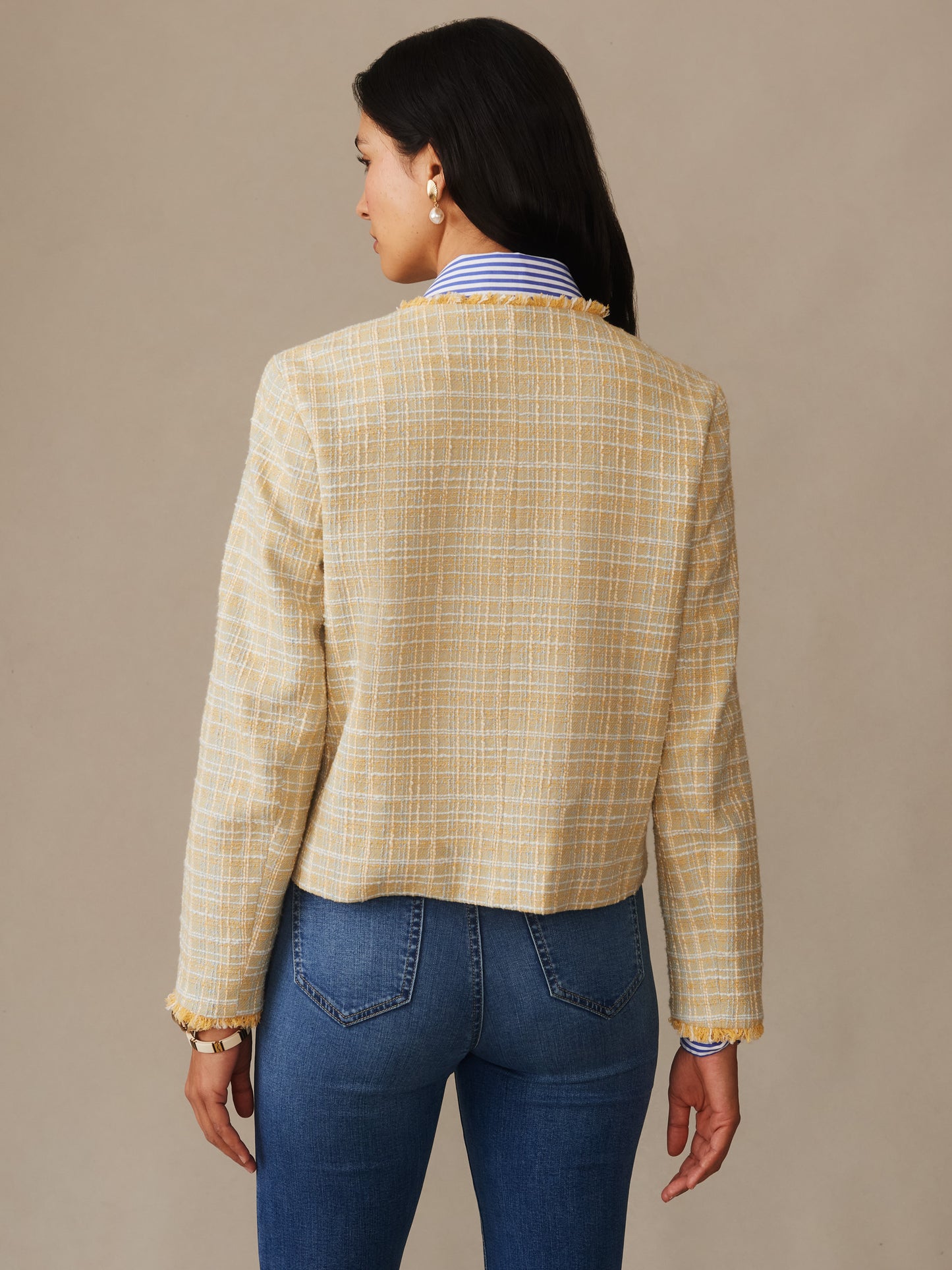 Woman wearing a mustard and off-white textured boucle jacket with mini window pane pattern, paired with blue jeans and pearl earrings, showcasing J.McLaughlin's Abigail Bouclé Jacket in Mini Window Pane, effortlessly stylish with enduring designs and innovative fabrics, a destination for defining style. Life, Well-Lived.