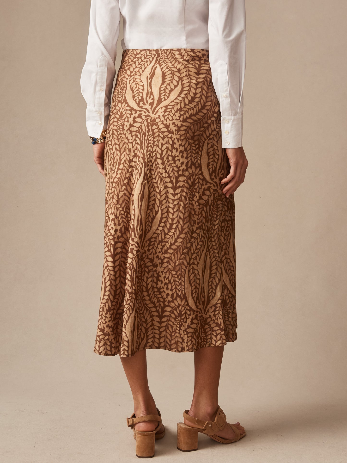 Back view of a person wearing the Adelyn Skirt in Coral Current Bias by J.McLaughlin, featuring an effortlessly stylish printed skirt paired with a classic white blouse and tan sandals, showcasing enduring designs and a legacy of timeless fashion from a destination for defining style. Life, Well-Lived.
