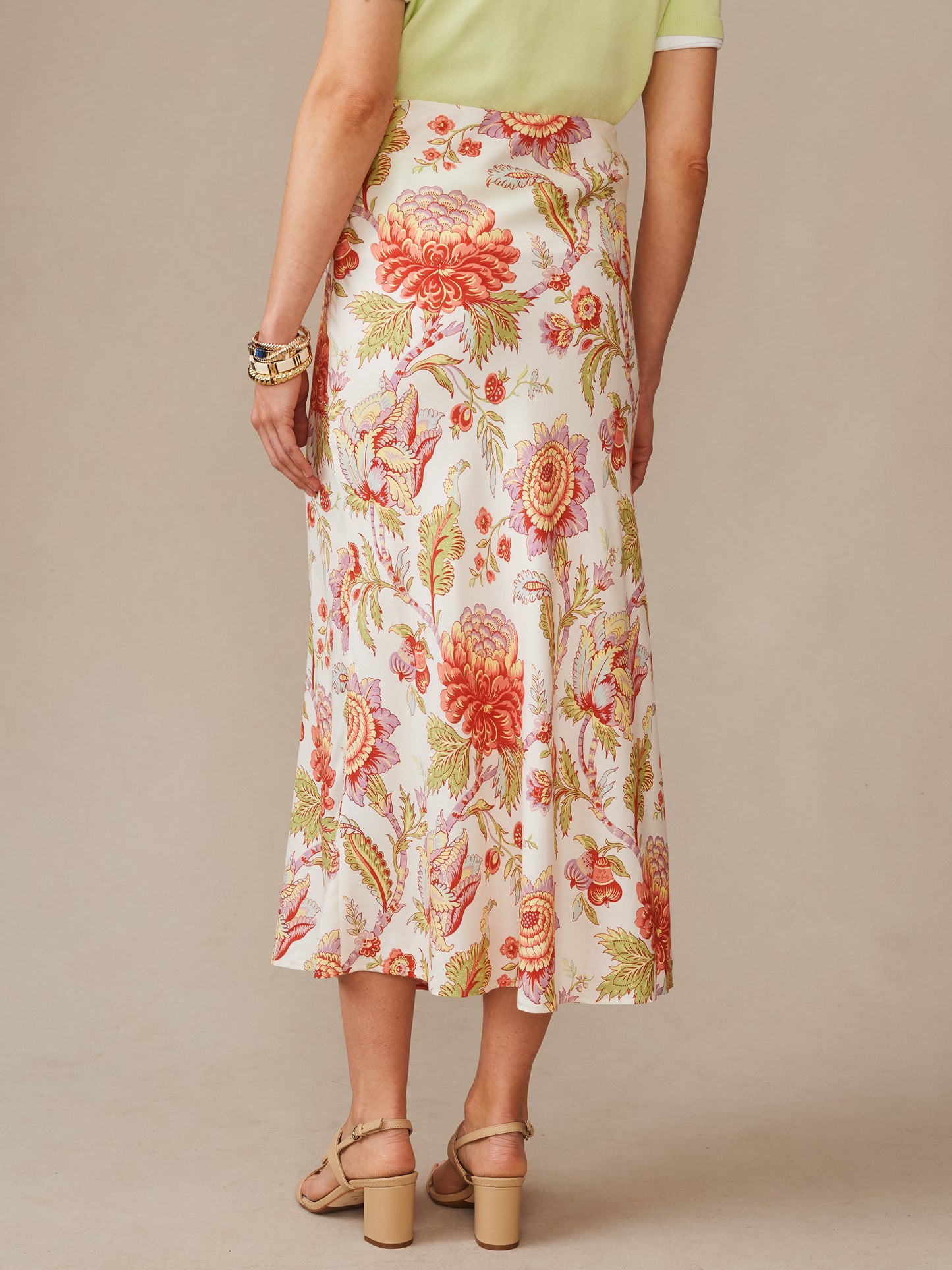 Back view of a woman wearing the Adelyn Silk Blend Skirt in Cerulean Garden Bias by J.McLaughlin, featuring a floral pattern in warm tones, paired with sandals and bracelets, effortlessly stylish with enduring designs and innovative fabrics, a destination for defining style. Life, Well-Lived.