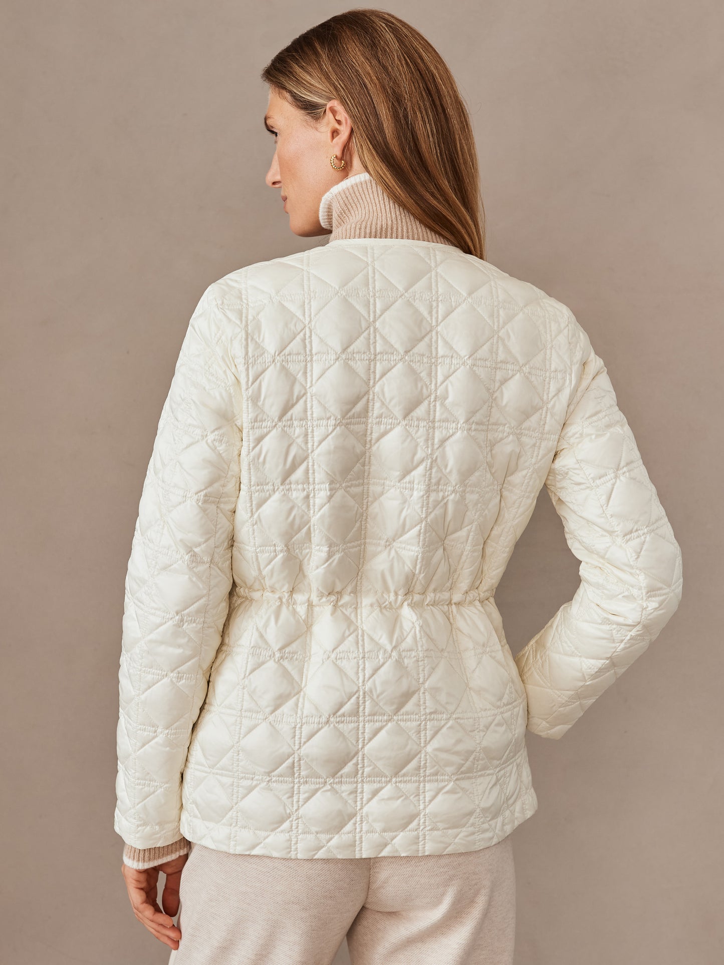 Woman wearing an egret white Ambrose Quilted Puffer by J.McLaughlin, styled with a beige turtleneck and pants, showcasing effortlessly stylish, enduring designs in innovative fabrics for a legacy of timeless fashion. A destination for defining style. Life, Well-Lived.