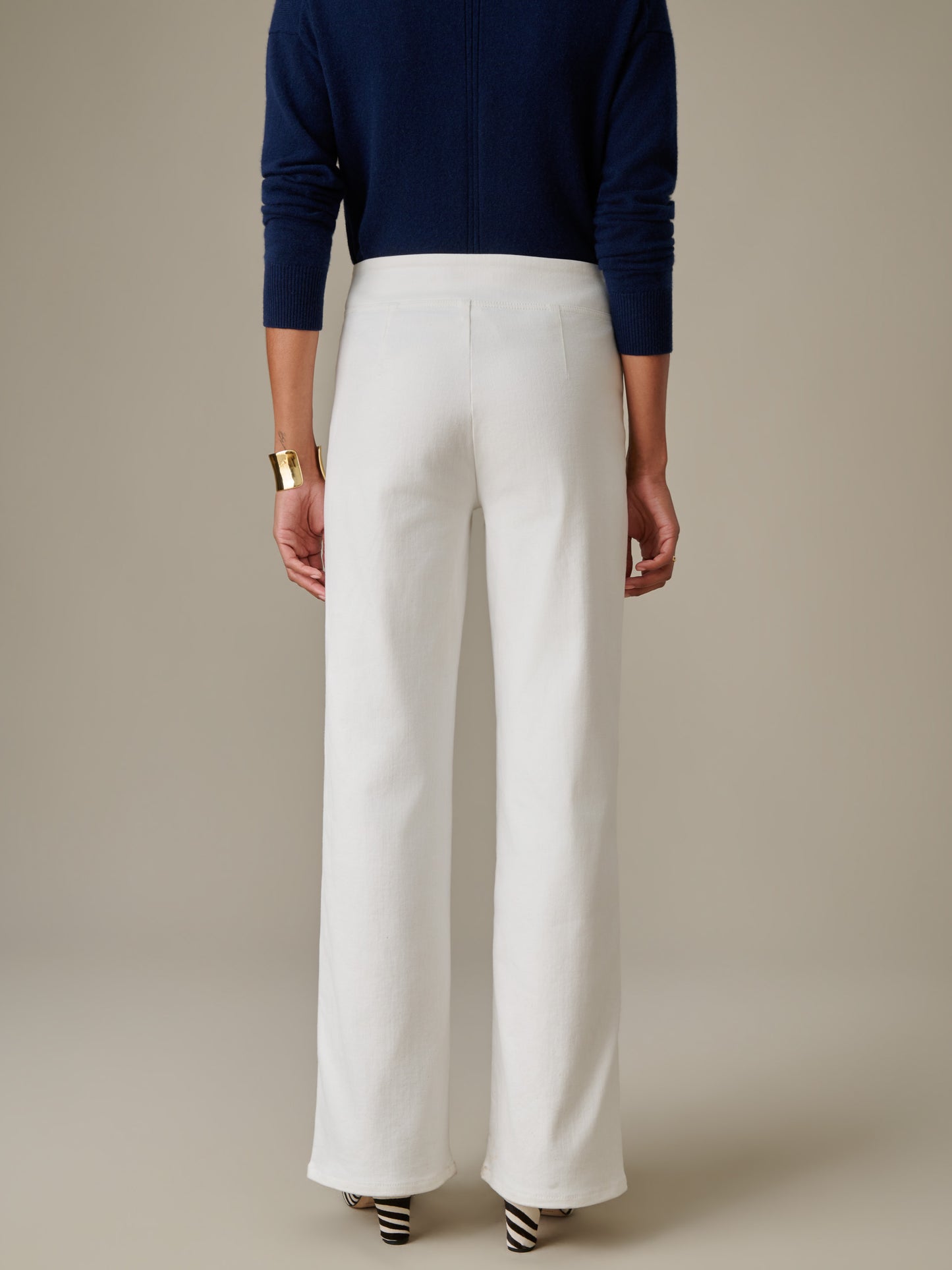 Woman wearing white Anderson Jeans from J.McLaughlin paired with a navy blue sweater and a gold cuff bracelet, showcasing effortlessly stylish, enduring design.
