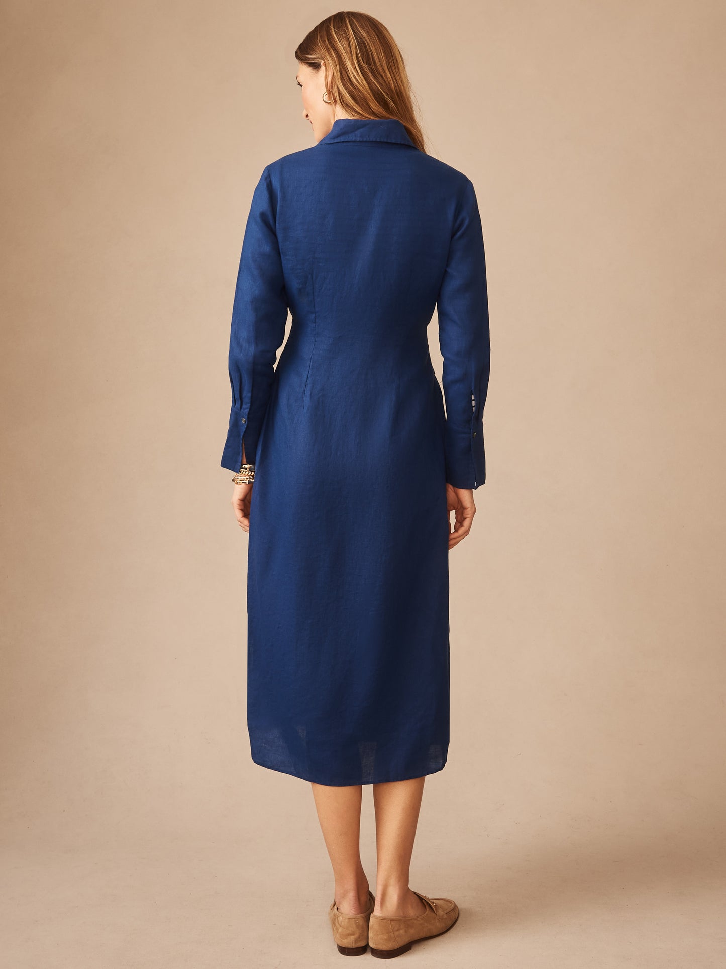 A woman stands facing away wearing the Orla Linen Dress by J.McLaughlin in a classic navy linen fabric, showcasing an effortlessly stylish, enduring design with innovative fabrics.