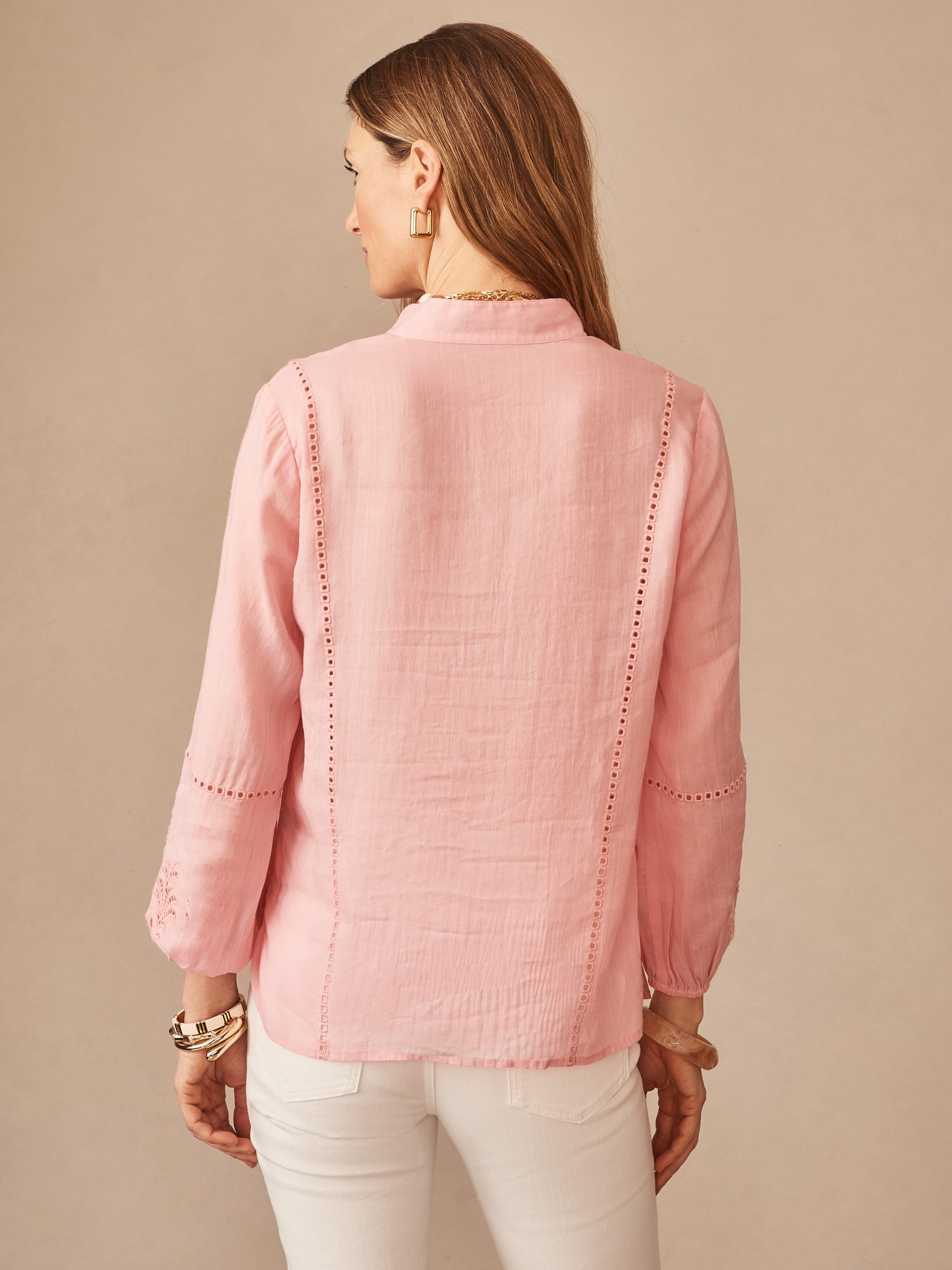 A woman models the Varsha Blouse by J.McLaughlin in soft pink quartz, featuring delicate eyelet details on sleeves and back, showcasing effortlessly stylish, enduring designs with a legacy of timeless fashion. A destination for defining style. Life, Well-Lived.