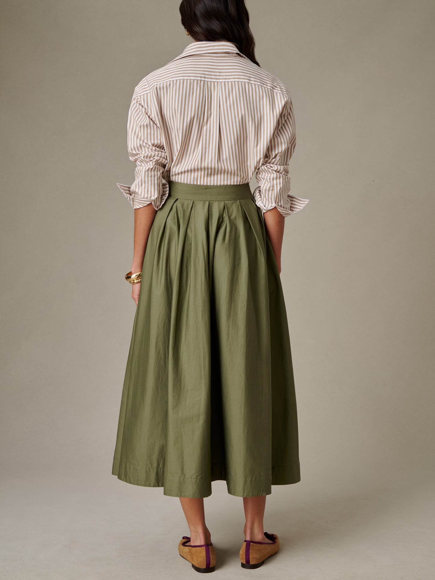 Woman wearing an olive green Arabella Skirt by J.McLaughlin paired with a striped shirt and brown sandals, showcasing timeless, effortlessly stylish design.