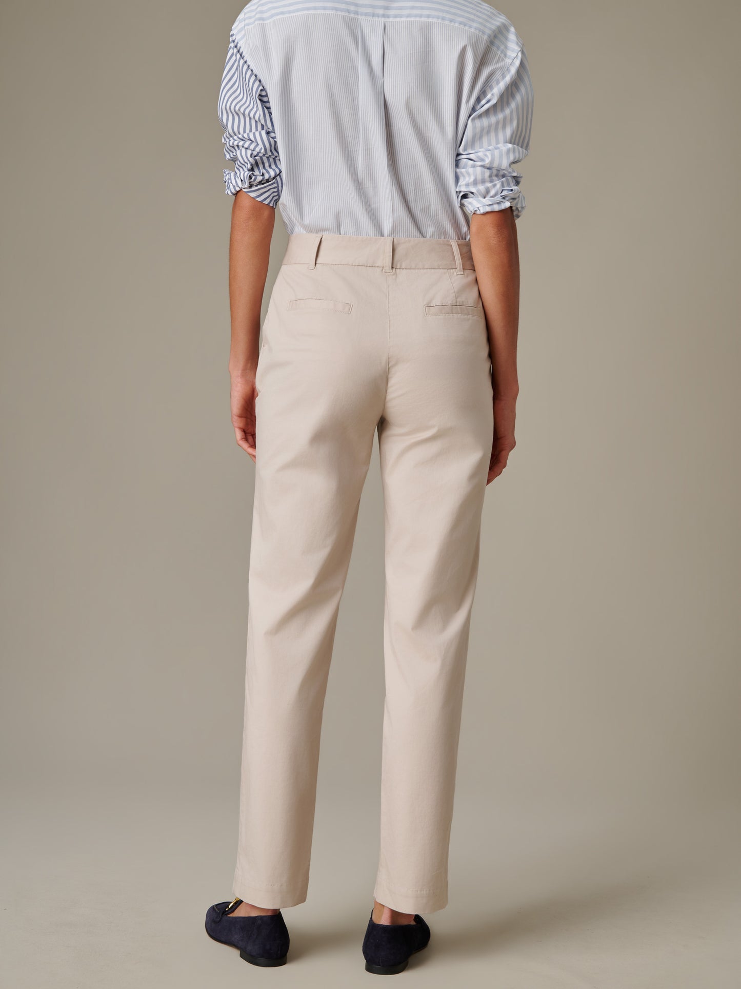 Back view of a person wearing beige Avery Cotton Chino Pants by J.McLaughlin, paired with a striped shirt and navy slip-on shoes, highlighting timeless style and craftsmanship.