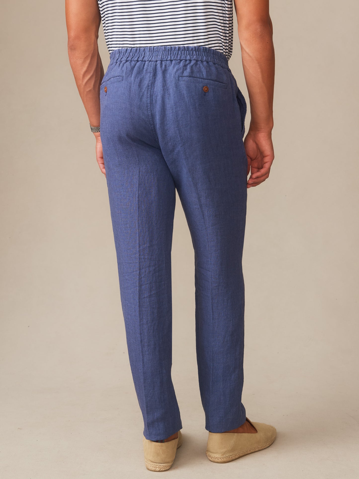 A rear view of a male model wearing Bleeker Linen Fancy Pants in deep denim blue by J.McLaughlin, showcasing effortlessly stylish pants crafted from innovative fabrics for enduring designs.