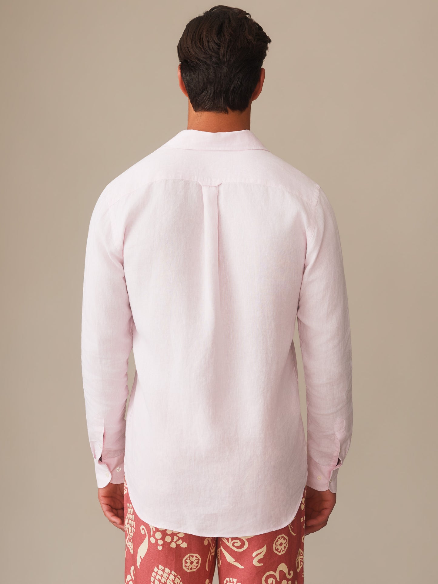 Man wearing a light pink Gramercy Linen Shirt by J.McLaughlin paired with patterned shorts, showcasing effortlessly stylish, enduring designs and innovative fabrics for a life well-lived.