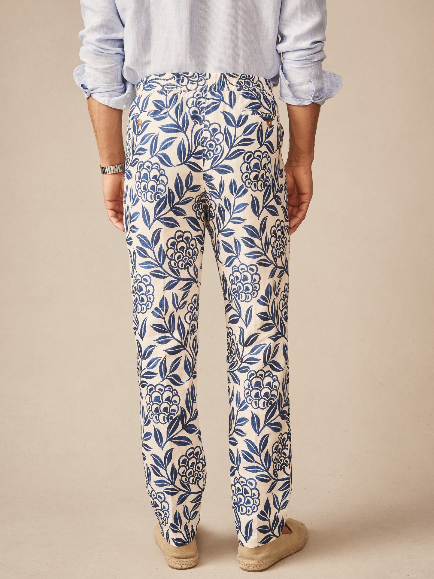 Back view of a person wearing Bleeker Linen Fancy Pants in Modern Dahlia featuring a blue floral linen pattern, paired with a light blue shirt and casual shoes, embodying J.McLaughlin’s effortlessly stylish and enduring designs, crafted with innovative fabrics and a legacy of timeless fashion. A destination for defining style. Life, Well-Lived.
