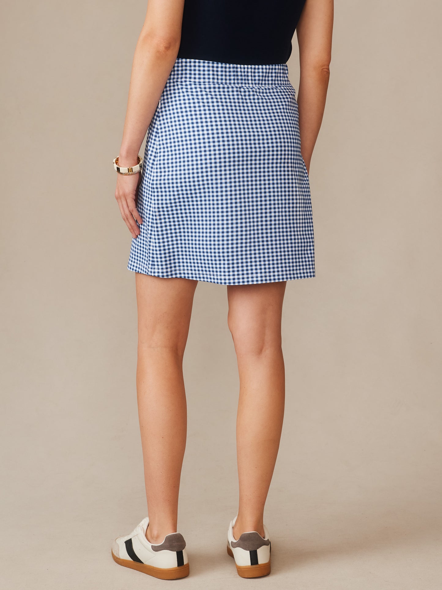 Back view of a model wearing the Briana Skort in Midi Cabana Gingham by J.McLaughlin, featuring effortlessly stylish, enduring designs in navy and white classic gingham, a destination for defining style. Life, Well-Lived.