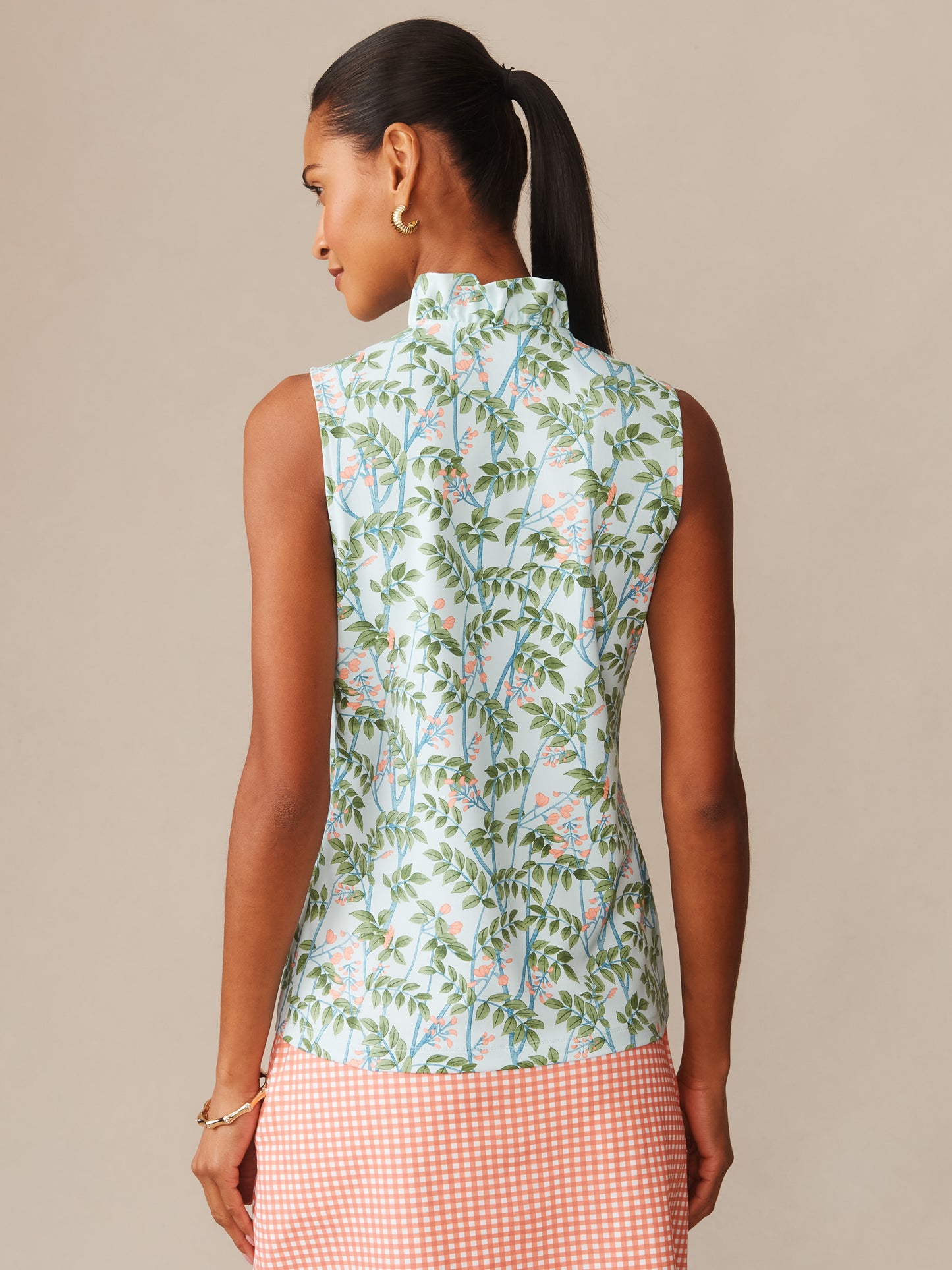 Woman seen from behind wearing a sleeveless top with a green leafy and floral pattern paired with a coral gingham skirt, showcasing the Kate Sleeveless Ruffle Top in Neo Blooming Vines by J.McLaughlin, effortlessly stylish with enduring designs and innovative fabrics.
