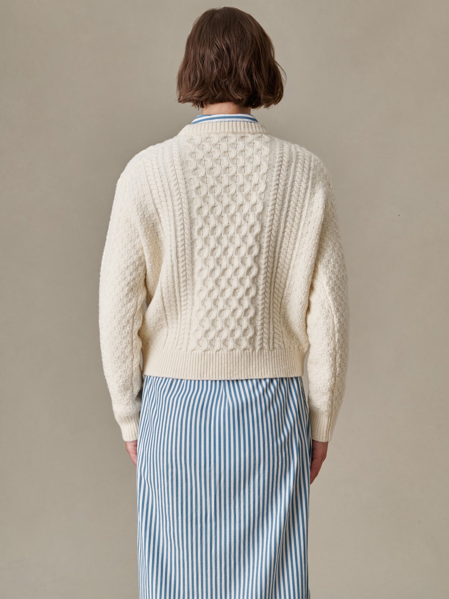 Back view of a person wearing a textured cream Brigette Sweater by J.McLaughlin paired with a blue and white striped skirt, showcasing classic and enduring design.