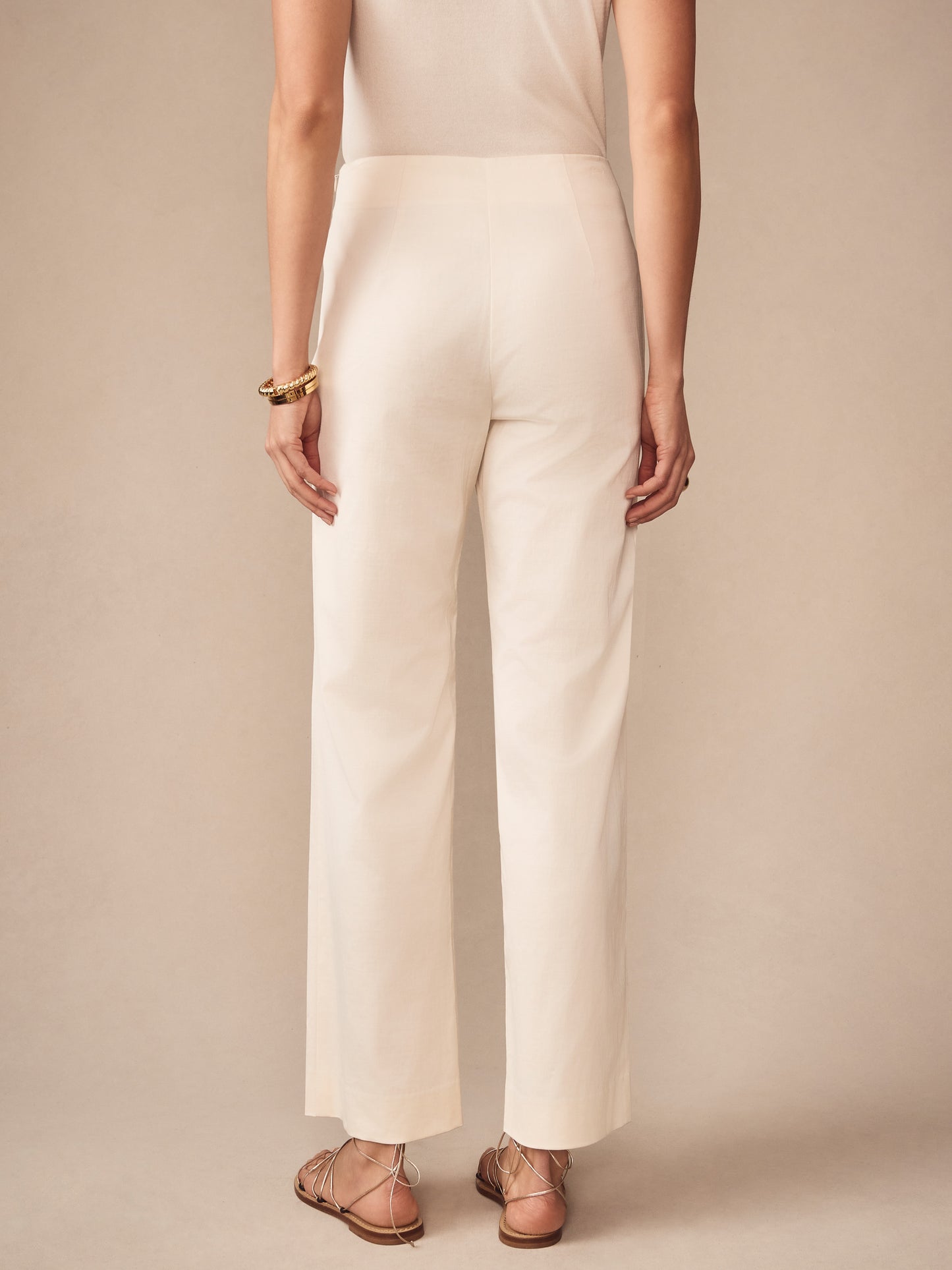 Back view of a woman wearing cream Carter Dupioni Cotton Pants by J.McLaughlin, paired with tan sandals and gold bangles, showcasing effortlessly stylish, enduring designs in innovative fabrics.