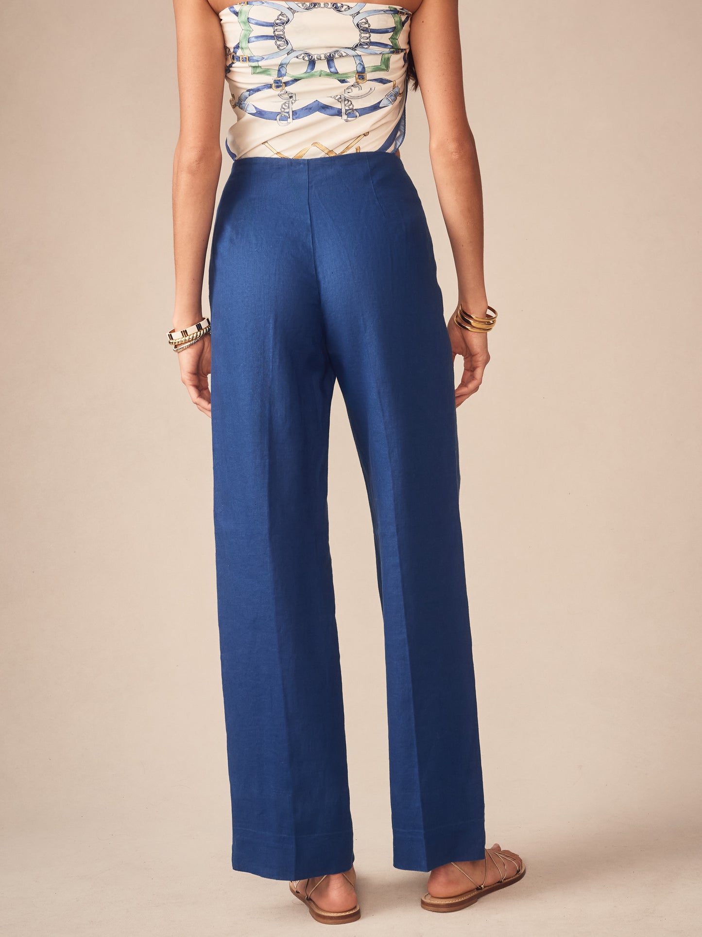 Woman wearing deep blue Carter Linen Pants by J.McLaughlin, styled with a patterned strapless top and sandals, showcasing effortlessly stylish, enduring designs in luxurious linen fabric.