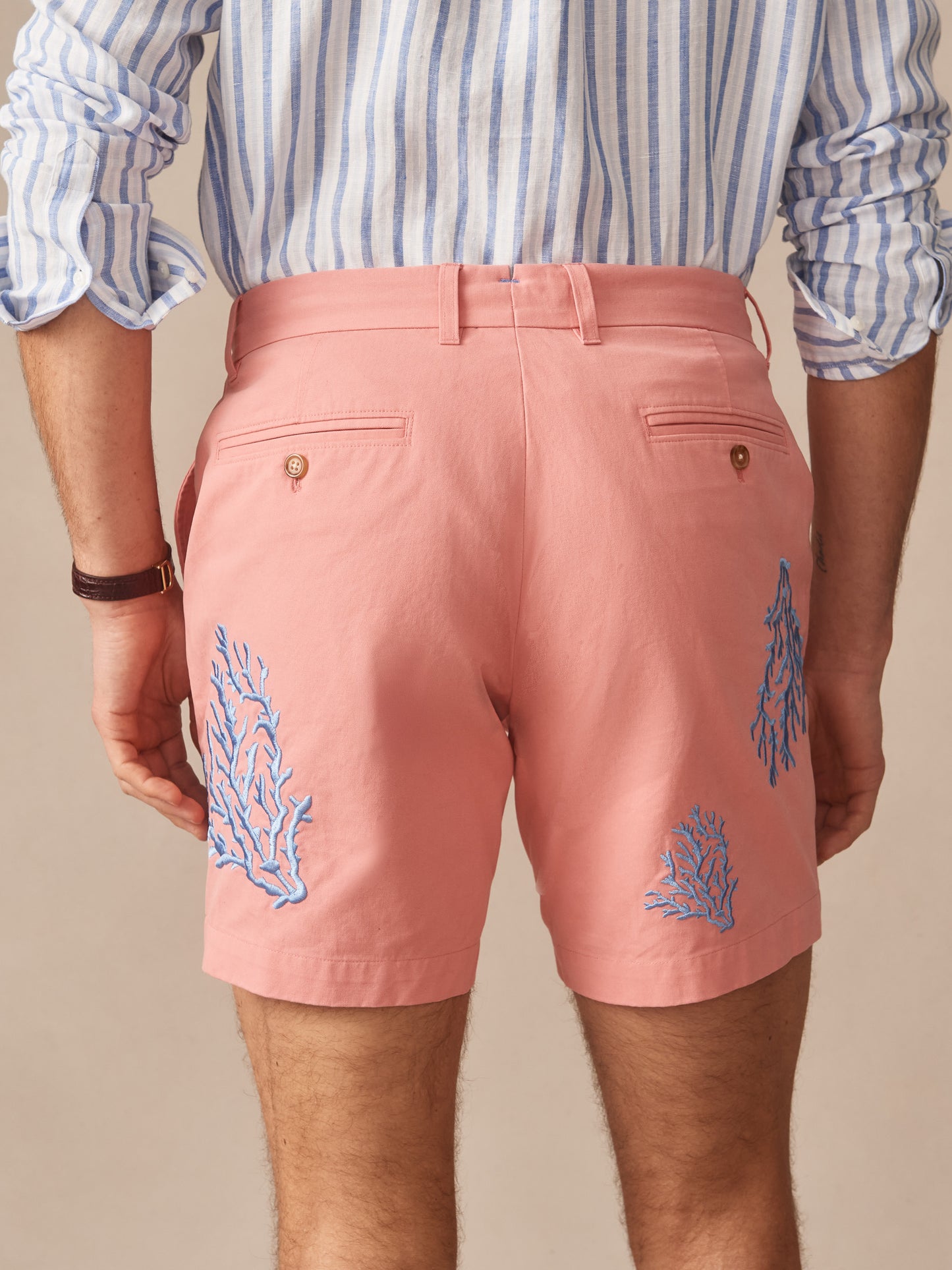 Man wearing Chatham Embroidered Shorts in Coral by J.McLaughlin, featuring blue coral embroidery on soft coral fabric, paired with a classic striped shirt, showcasing effortlessly stylish, enduring designs and innovative fabrics. A destination for defining style. Life, Well-Lived.