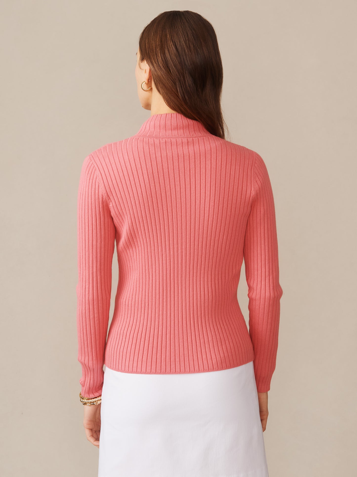 A woman wearing a ribbed pink Clemence Zip Cardigan by J.McLaughlin, paired with a white skirt, showcasing effortlessly stylish, enduring designs and innovative fabrics from a destination for defining style. Life, Well-Lived.