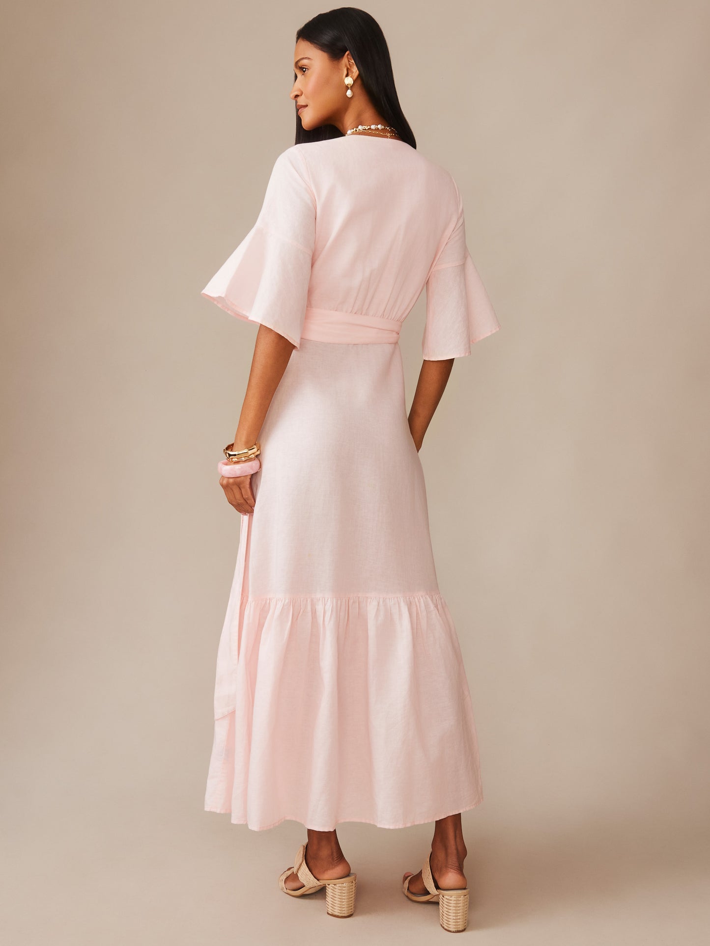 Woman wearing a light blush pink Emily Linen Blend Wrap Dress by J.McLaughlin with flared sleeves and a flowing skirt, embodying effortlessly stylish and enduring designs.