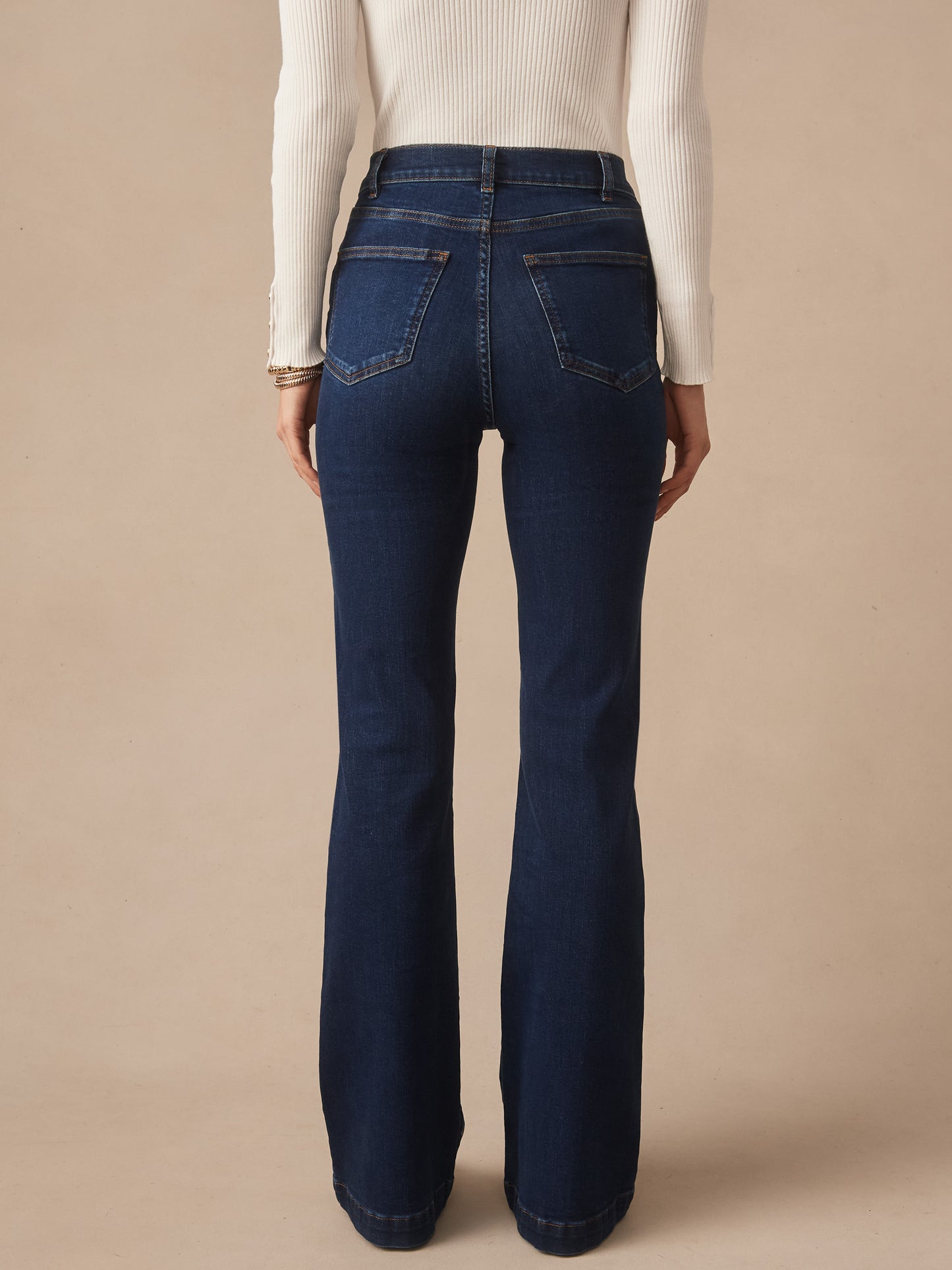 Back view of a woman wearing Domino Jeans by J.McLaughlin in dark denim, paired with a white ribbed long sleeve top, showcasing effortlessly stylish, enduring designs and a legacy of timeless fashion. A destination for defining style. Life, Well-Lived.