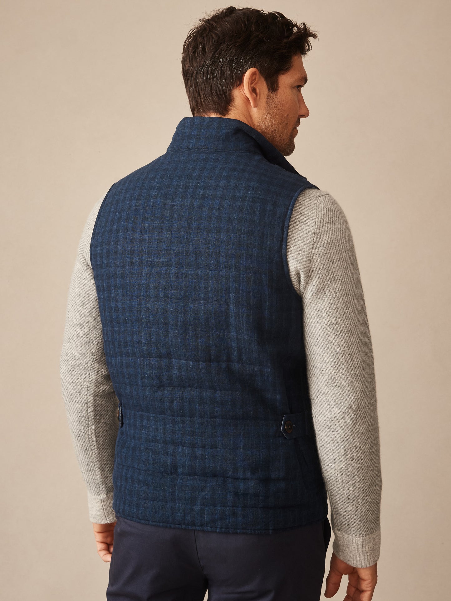 Man wearing a navy quilted vest with shadow plaid pattern over a light gray textured sweater, showcasing the back view of the Game Quilted Vest in Shadow Plaid by J.McLaughlin.