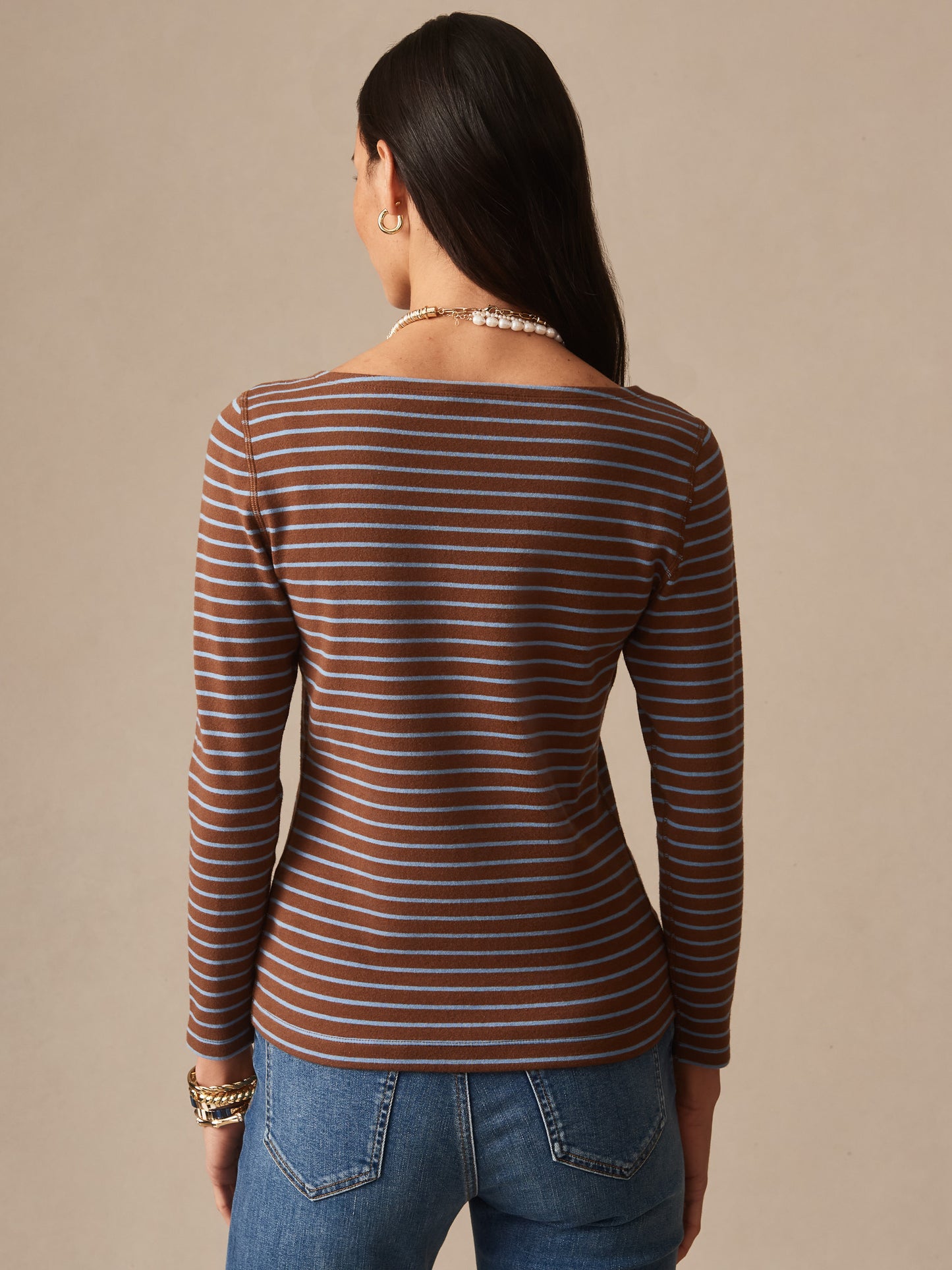 Woman wearing a brown and light blue striped Goldie Tee in Stripe by J.McLaughlin, paired with blue jeans, showcasing effortlessly stylish, enduring designs and innovative fabrics.