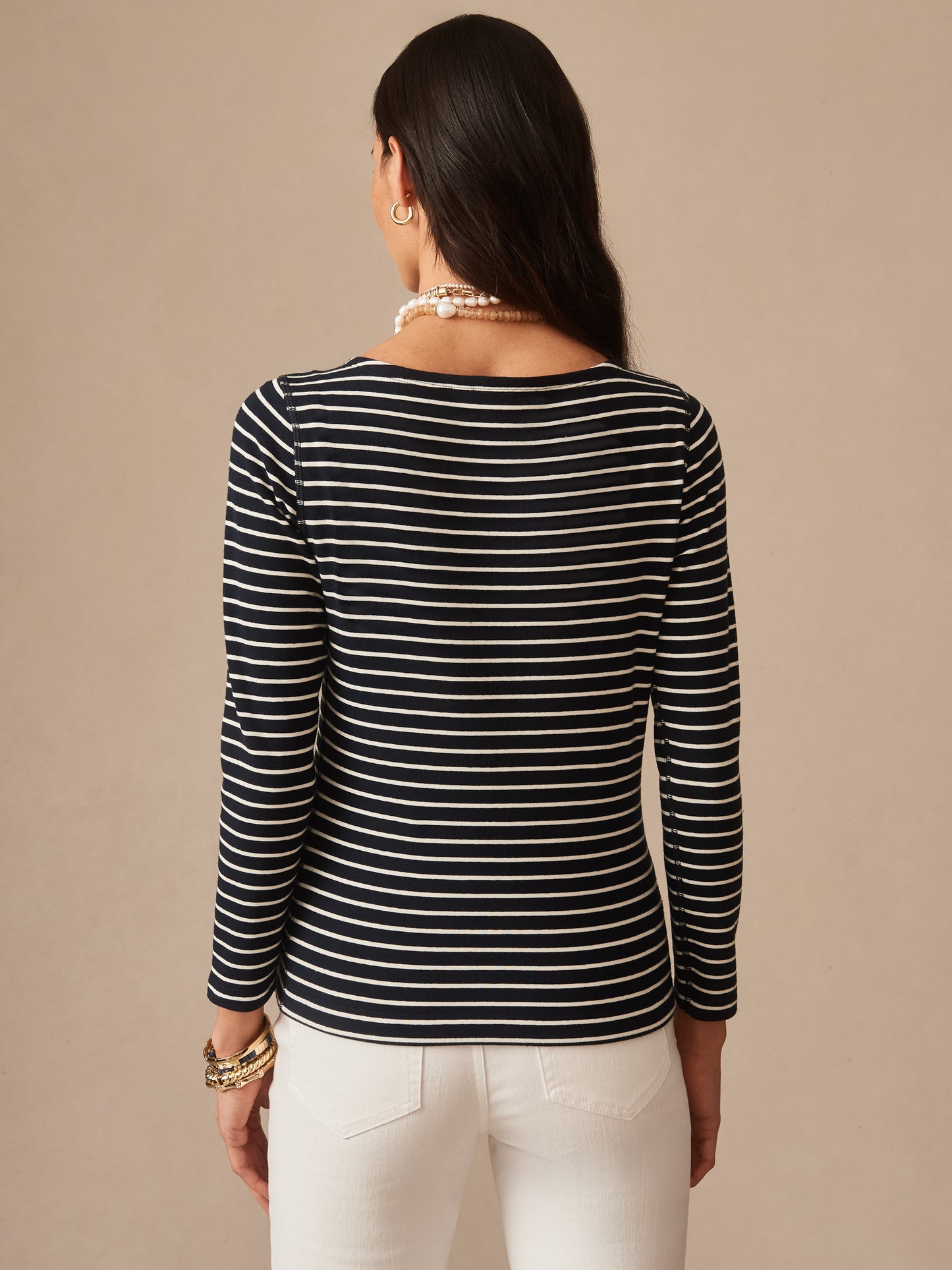 Woman wearing a navy and cream striped Goldie Tee in Stripe by J.McLaughlin, paired with white pants and accessories, showcasing effortlessly stylish, enduring designs.