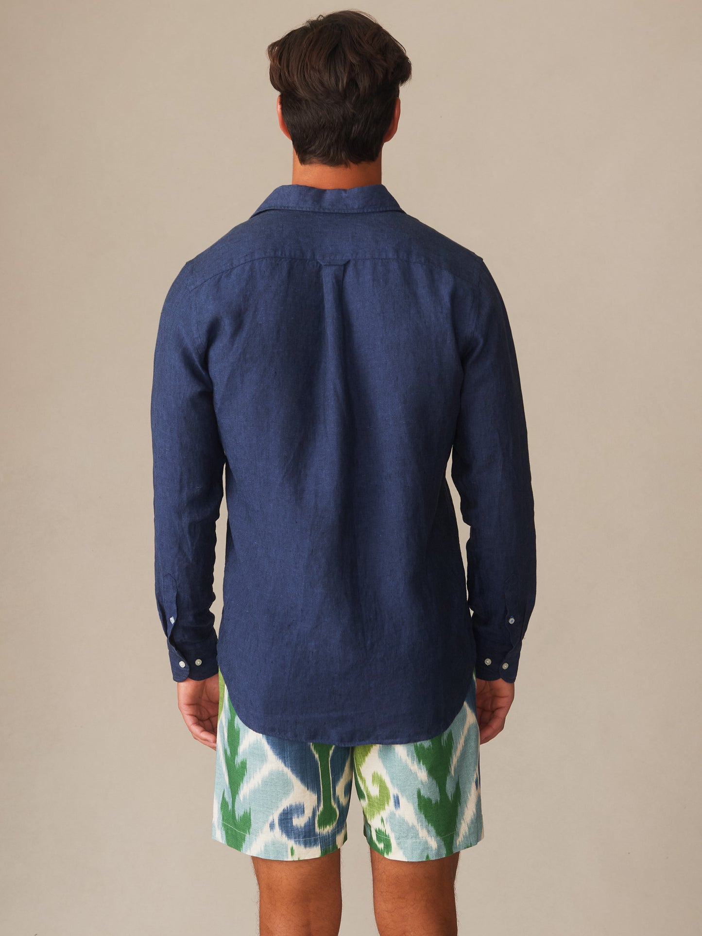 Man seen from the back wearing a navy Gramercy Linen Shirt by j.mclaughlin paired with patterned shorts, showcasing timeless and classic casual style.