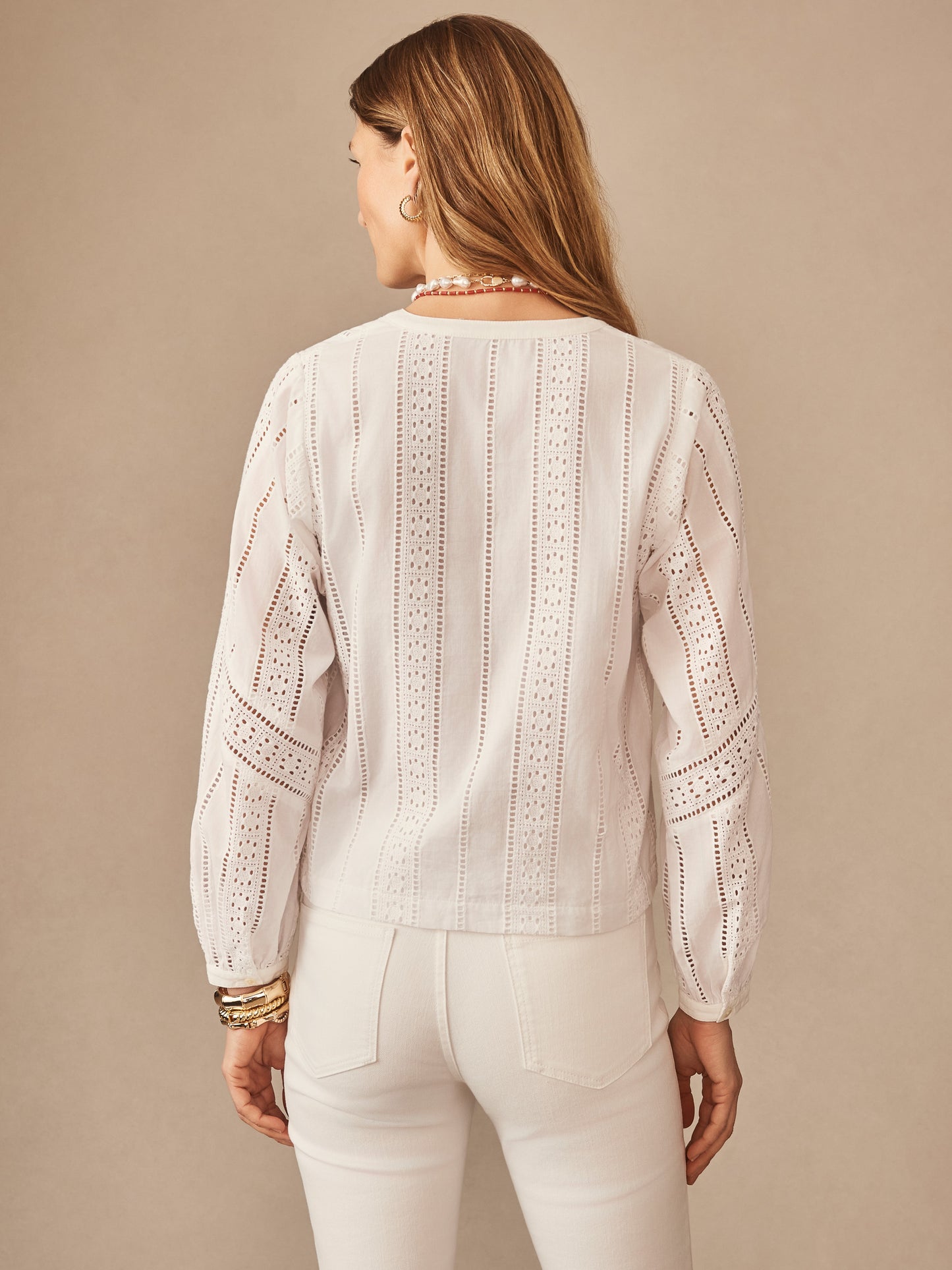 A woman seen from behind wearing the Hazel Blouse in Eyelet by J.McLaughlin, featuring intricate eyelet patterns and classic white fabric, embodying effortlessly stylish, enduring designs.