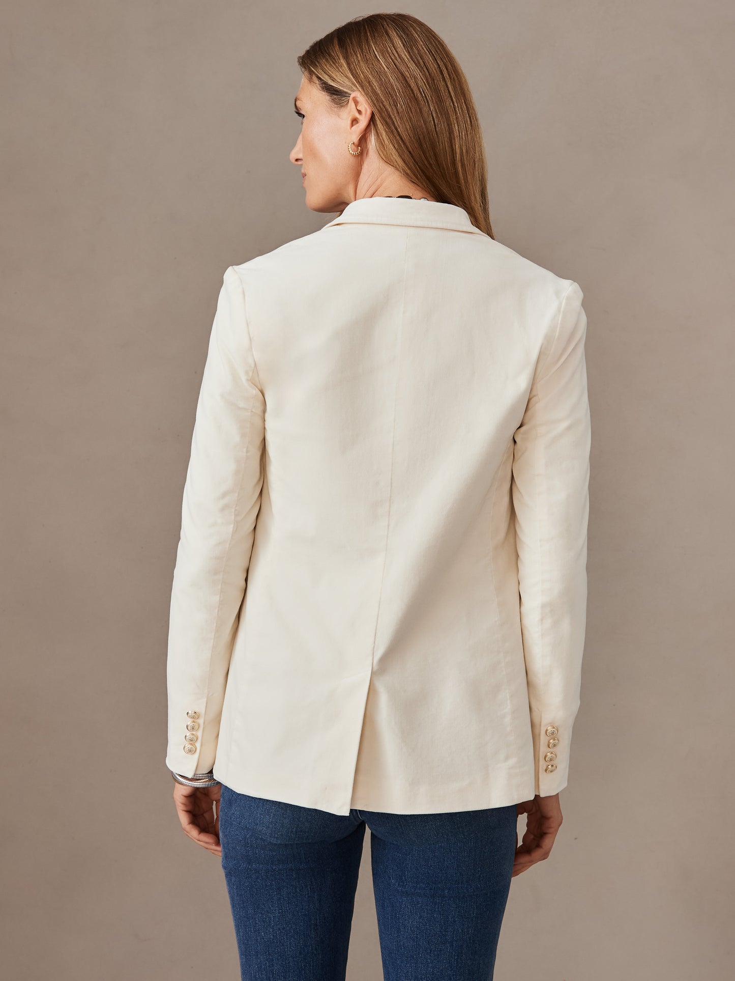 Woman wearing an egret white Ivette Velvet Blazer by J.McLaughlin, showcasing its tailored back and classic long sleeves, reflecting effortlessly stylish, enduring designs.