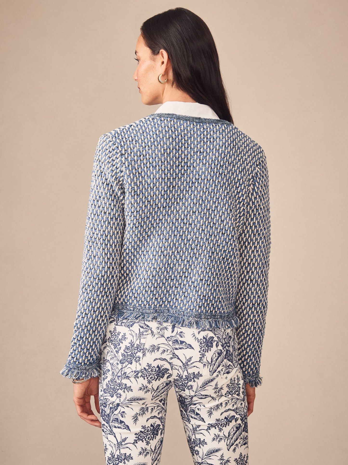 Woman wearing a blue and white textured Marceline Cardigan by J.McLaughlin paired with white pants featuring a blue floral print, showcasing effortlessly stylish, enduring designs.
