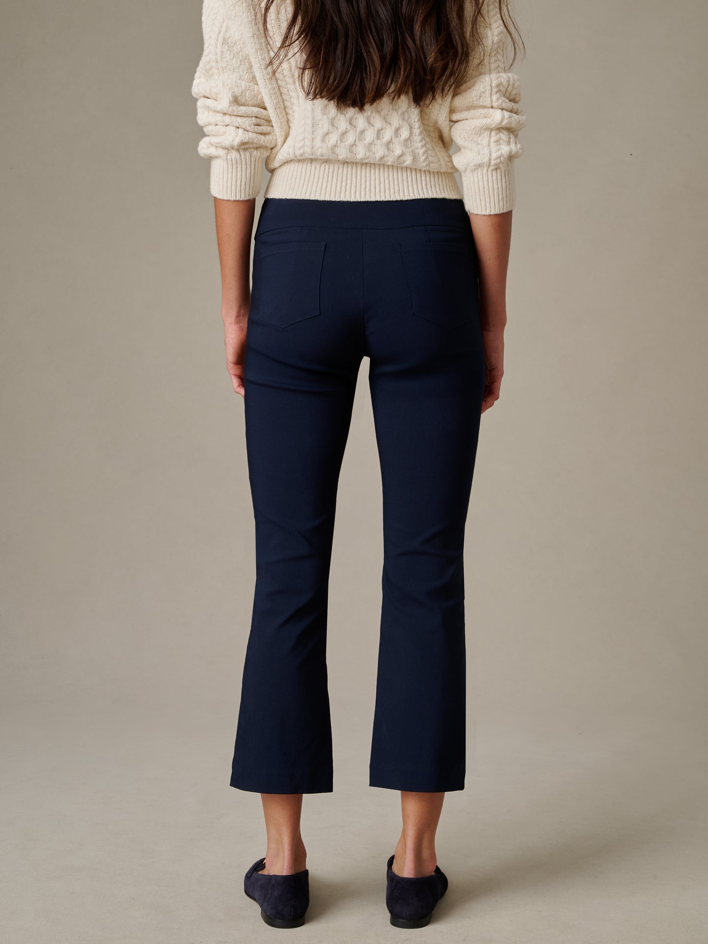 Rear view of a person wearing navy Ivy Pants by J.McLaughlin paired with a cream cable-knit sweater and navy flats, showcasing effortlessly stylish and enduring designs.