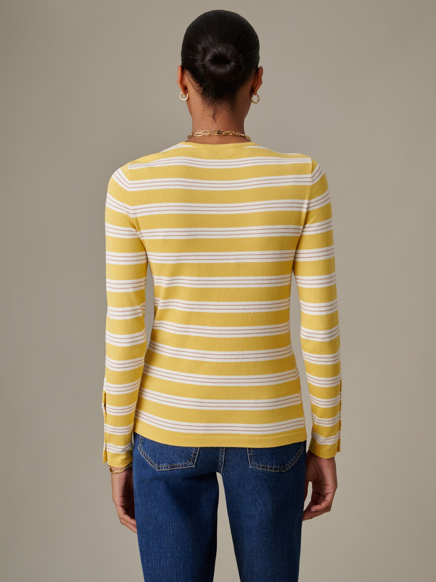 Woman seen from behind wearing a J.McLaughlin Jamey Sweater in Stripe in yellow and white, paired with classic blue jeans, showcasing timeless style and quality craftsmanship.