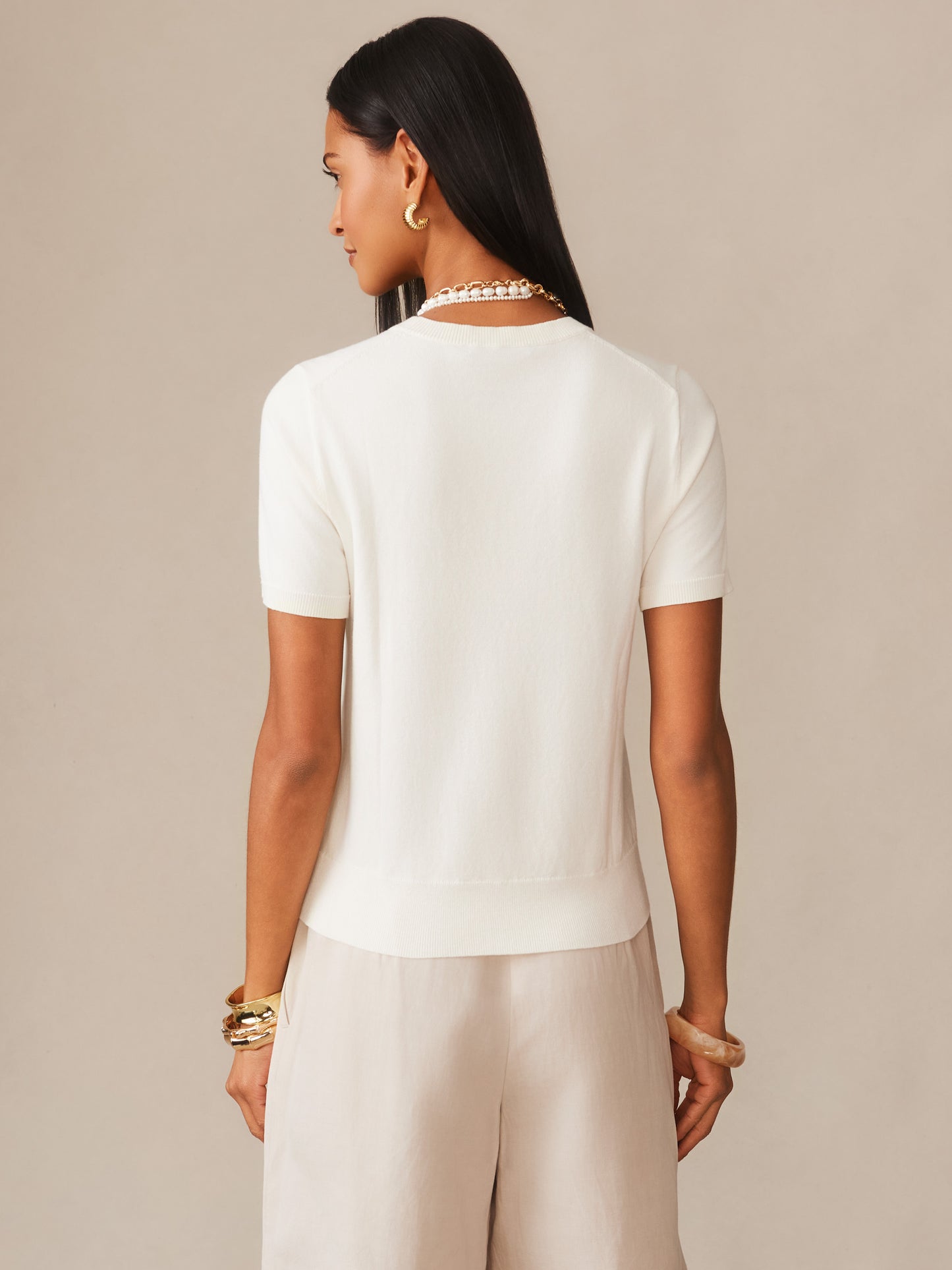 Woman wearing an ivory Joelle Sweater by J.McLaughlin, styled with elegant jewelry and neutral pants, showcasing effortlessly stylish and enduring designs for a life well-lived.