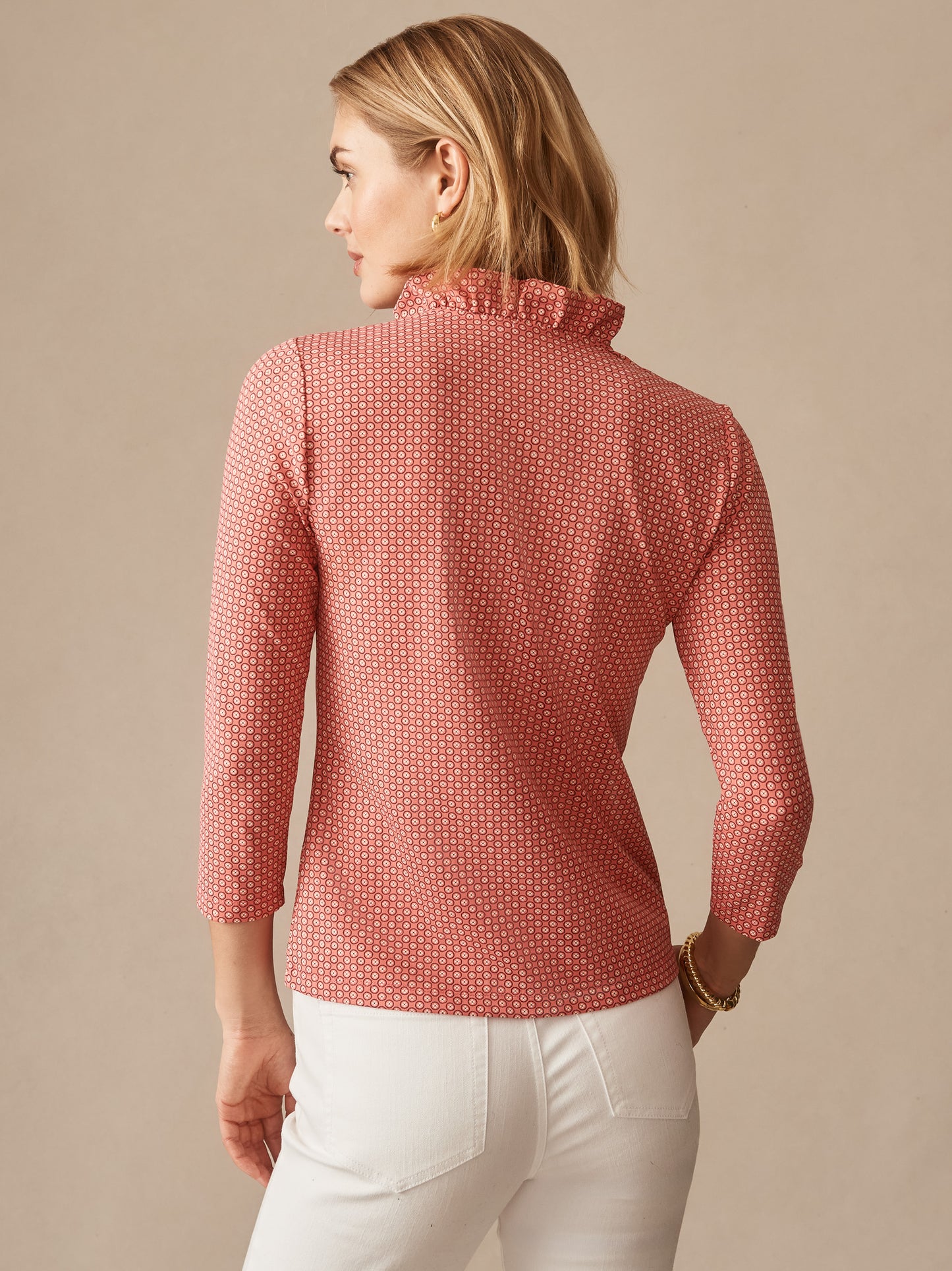 Woman wearing the Kate Ruffle Top in Bonneval by J.McLaughlin, featuring a subtle patterned fabric and ruffled neckline, paired with white pants, showcasing effortlessly stylish, enduring designs and innovative fabrics. A destination for defining style. Life, Well-Lived.