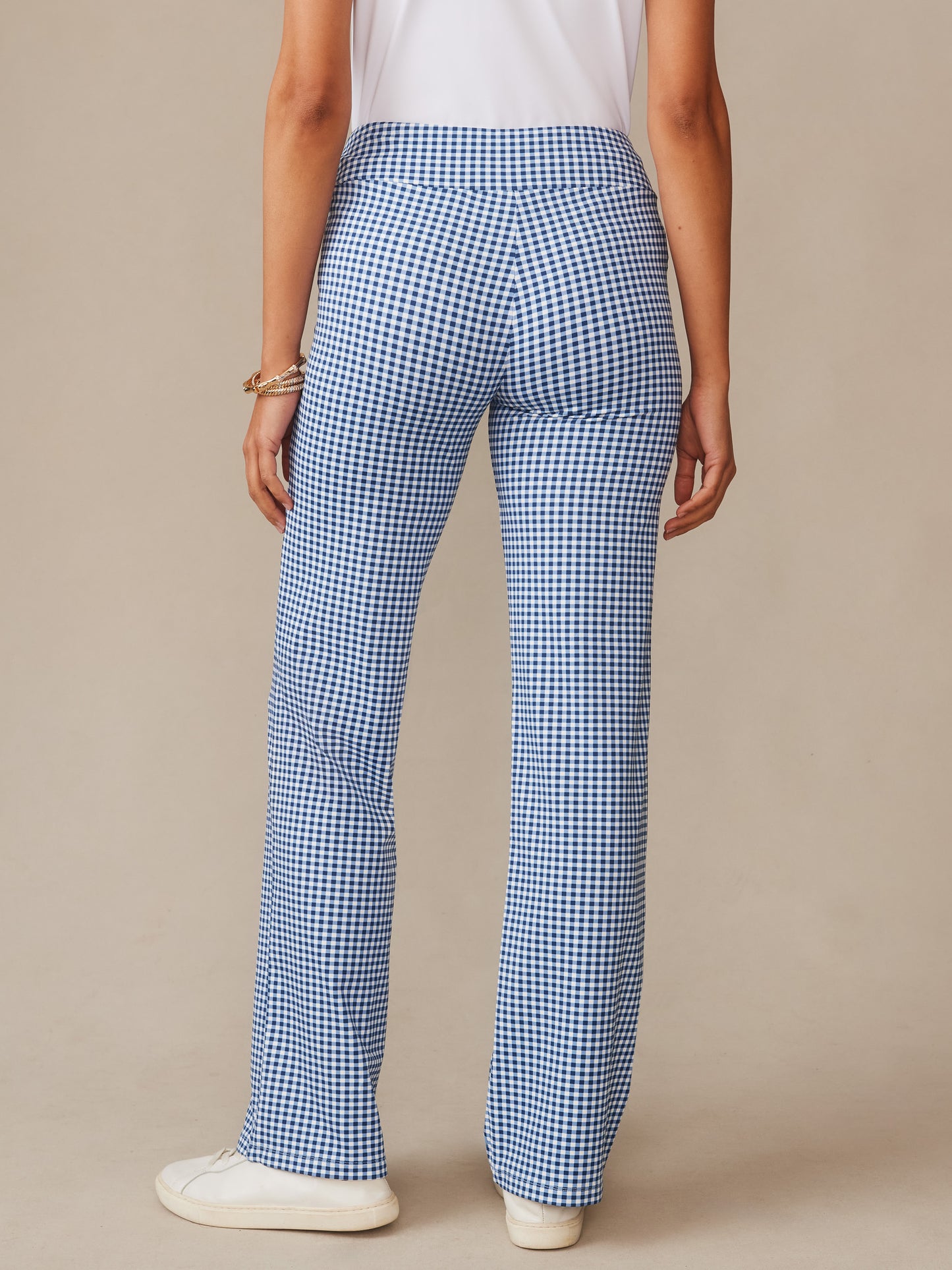 Back view of a model wearing J.McLaughlin Carmel Pants in Midi Cabana Gingham blue and white checked pants paired with a white top and sneakers, showcasing effortlessly stylish design and enduring appeal in innovative fabrics.