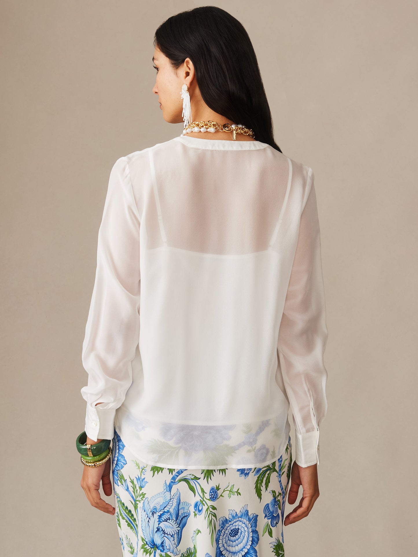 Woman modeling a Katherine Silk Chiffon Blouse from J.McLaughlin, featuring a sheer off-white fabric paired with a floral skirt, embodying effortlessly stylish, enduring designs.