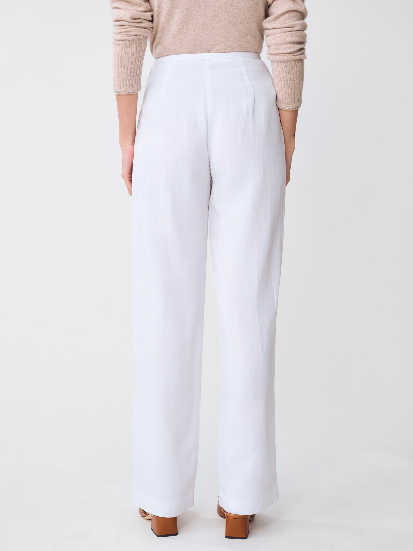 Back view of a model wearing J.McLaughlin Kilian Linen Blend Pants in white, paired with a beige sweater and brown shoes, showcasing effortlessly stylish, enduring designs with innovative fabrics in a legacy of timeless fashion. A destination for defining style. Life, Well-Lived.