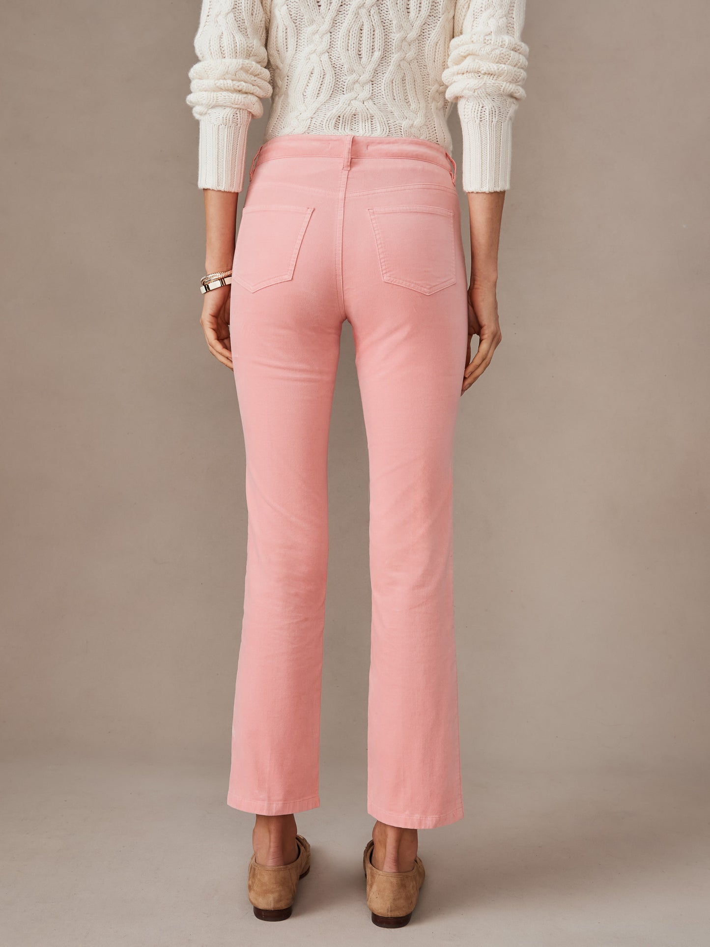 Woman wearing light coral Lenni Velvet Jeans by J.McLaughlin, paired with a white cable knit sweater and brown suede shoes, showcasing effortlessly stylish, enduring designs and innovative fabrics.