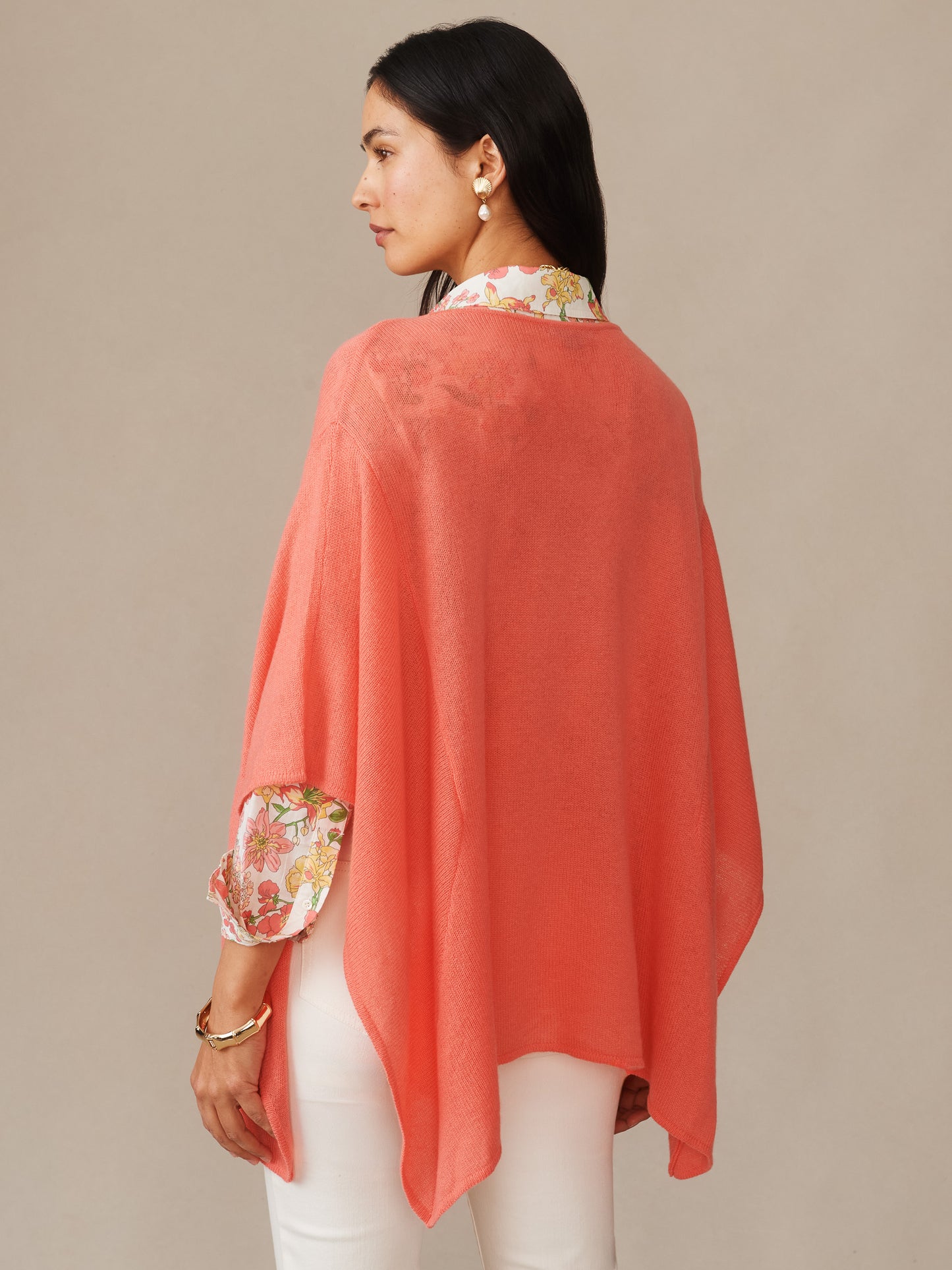 Woman wearing a coral Marin Cashmere Poncho by J.McLaughlin over a floral blouse, showcasing effortlessly stylish layering with enduring designs and innovative fabrics.