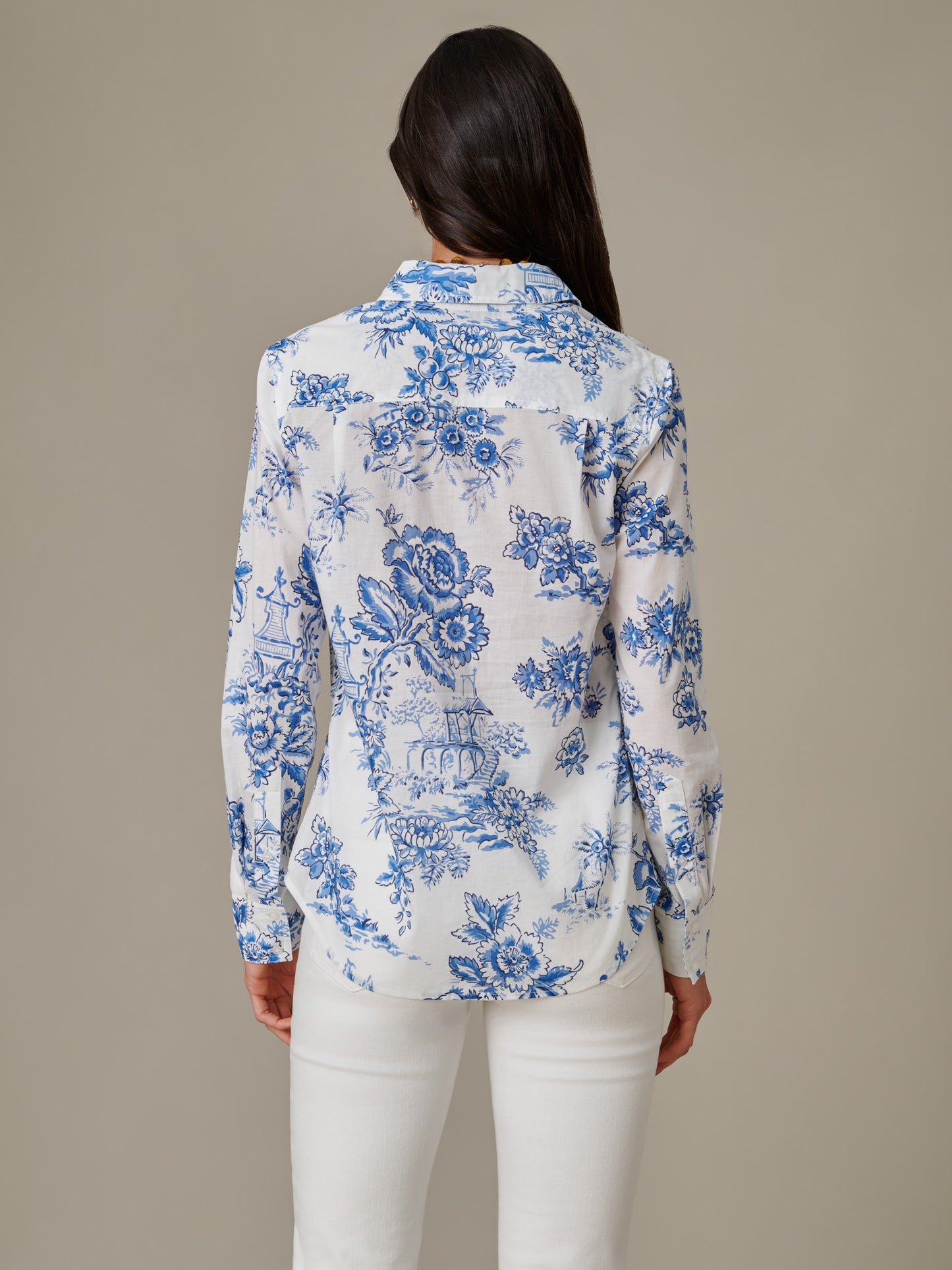 Woman seen from behind wearing the Lois Shirt in Antique Toile Stripe by J.McLaughlin, featuring a classic blue floral pattern on a white background, paired with white pants.