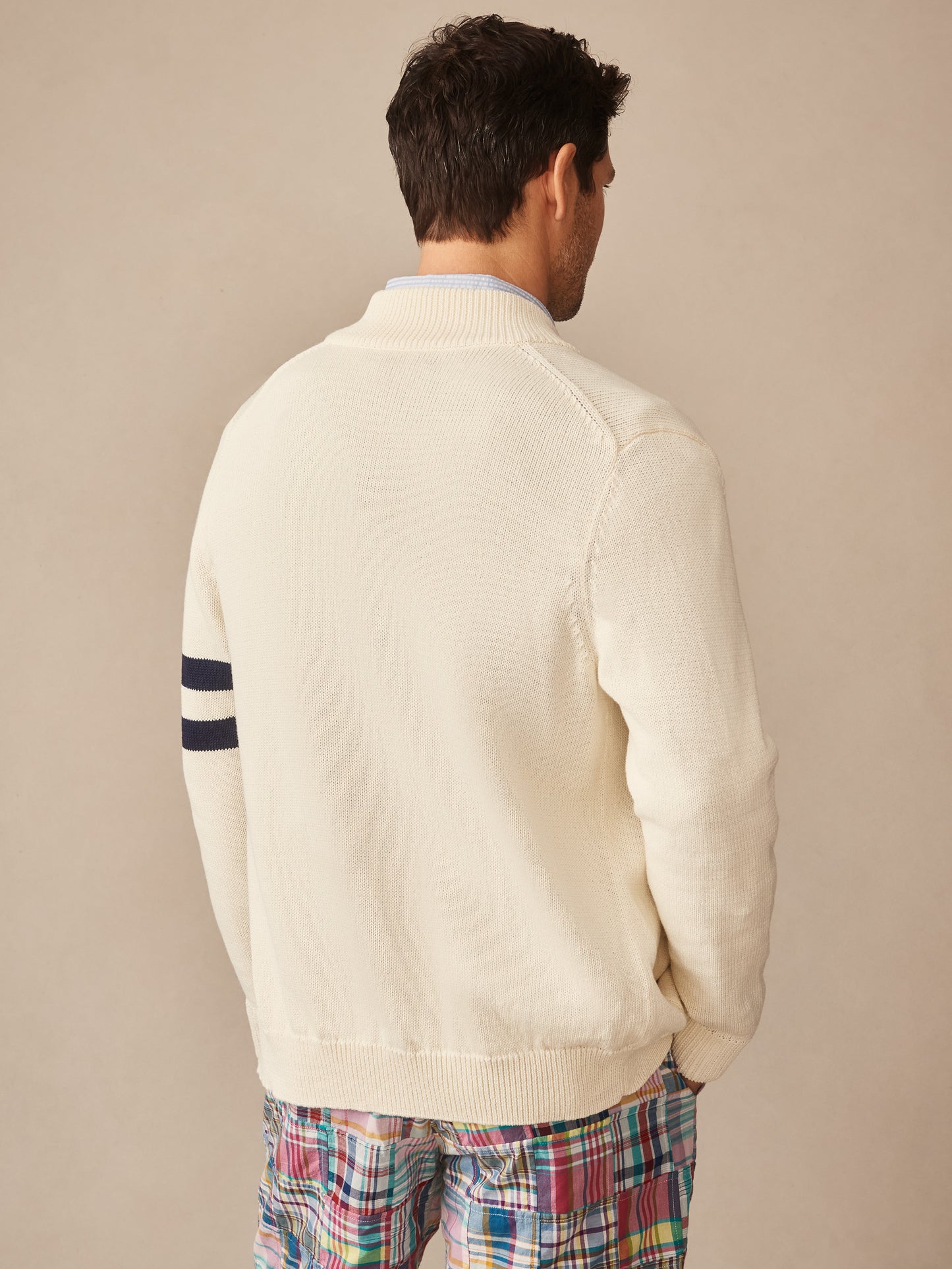Man wearing an off-white Lowell Sweater by J.McLaughlin featuring navy stripes on the sleeve, styled with colorful plaid pants against a neutral background.